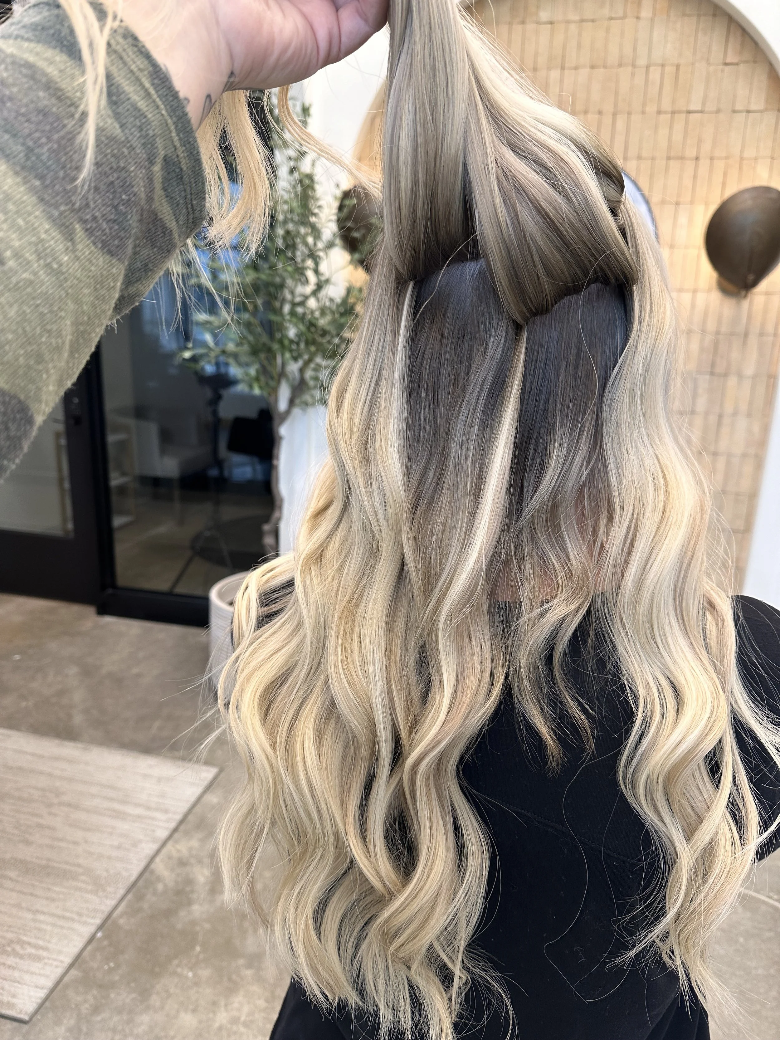 A person with long, wavy blonde hair, partially clipped back, at a hair salon.