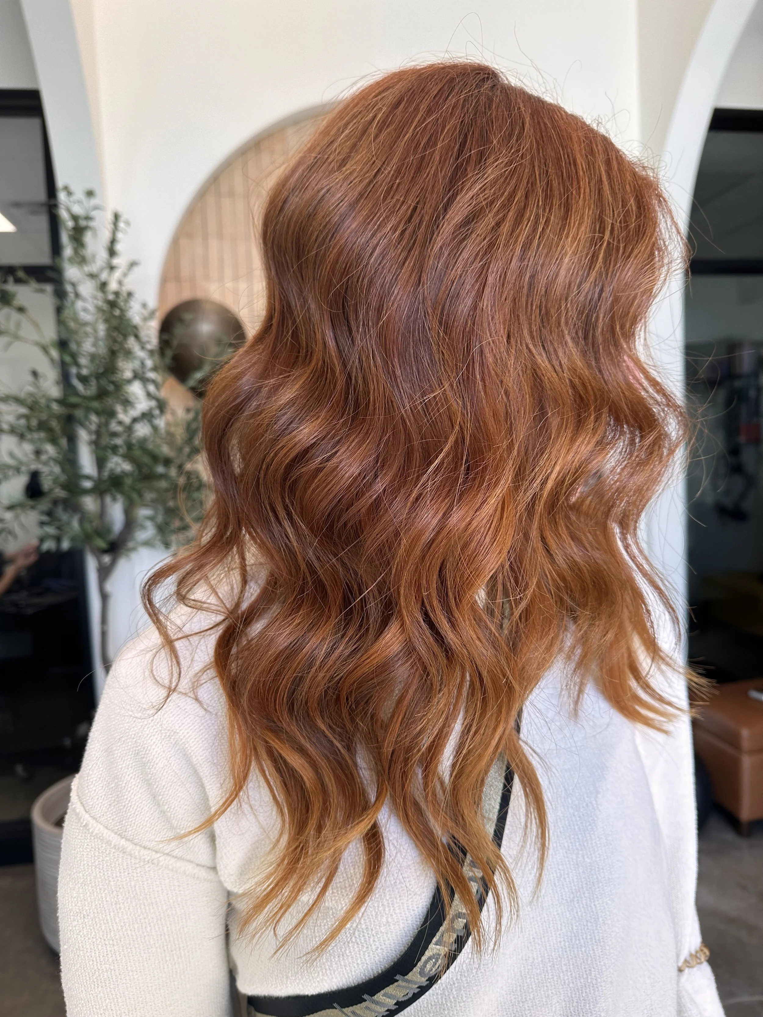 Side view of a woman with long, wavy, reddish-brown hair inside a salon.
