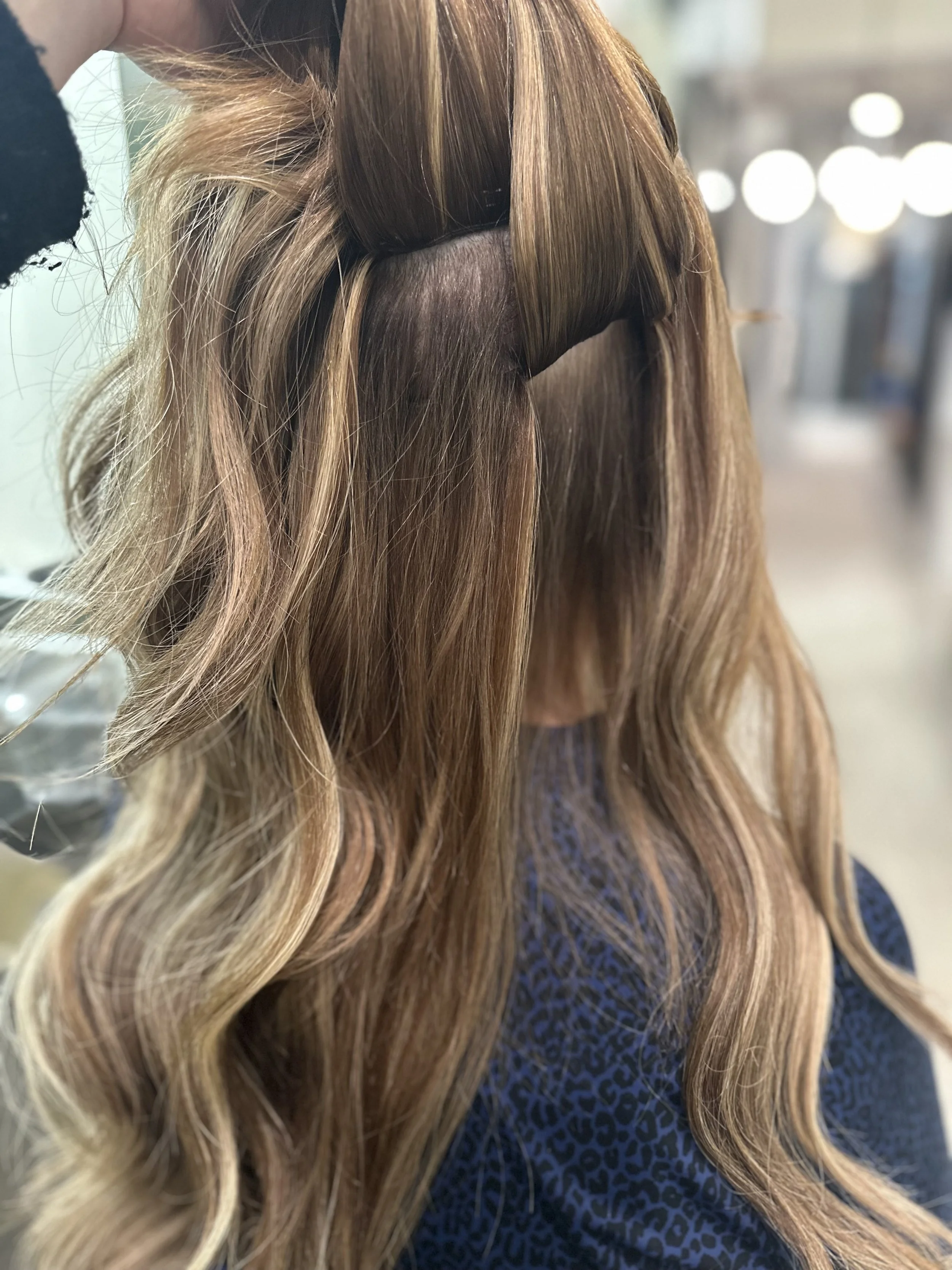 Side view of a woman with long, wavy, light brown hair getting a layered haircut at a salon.