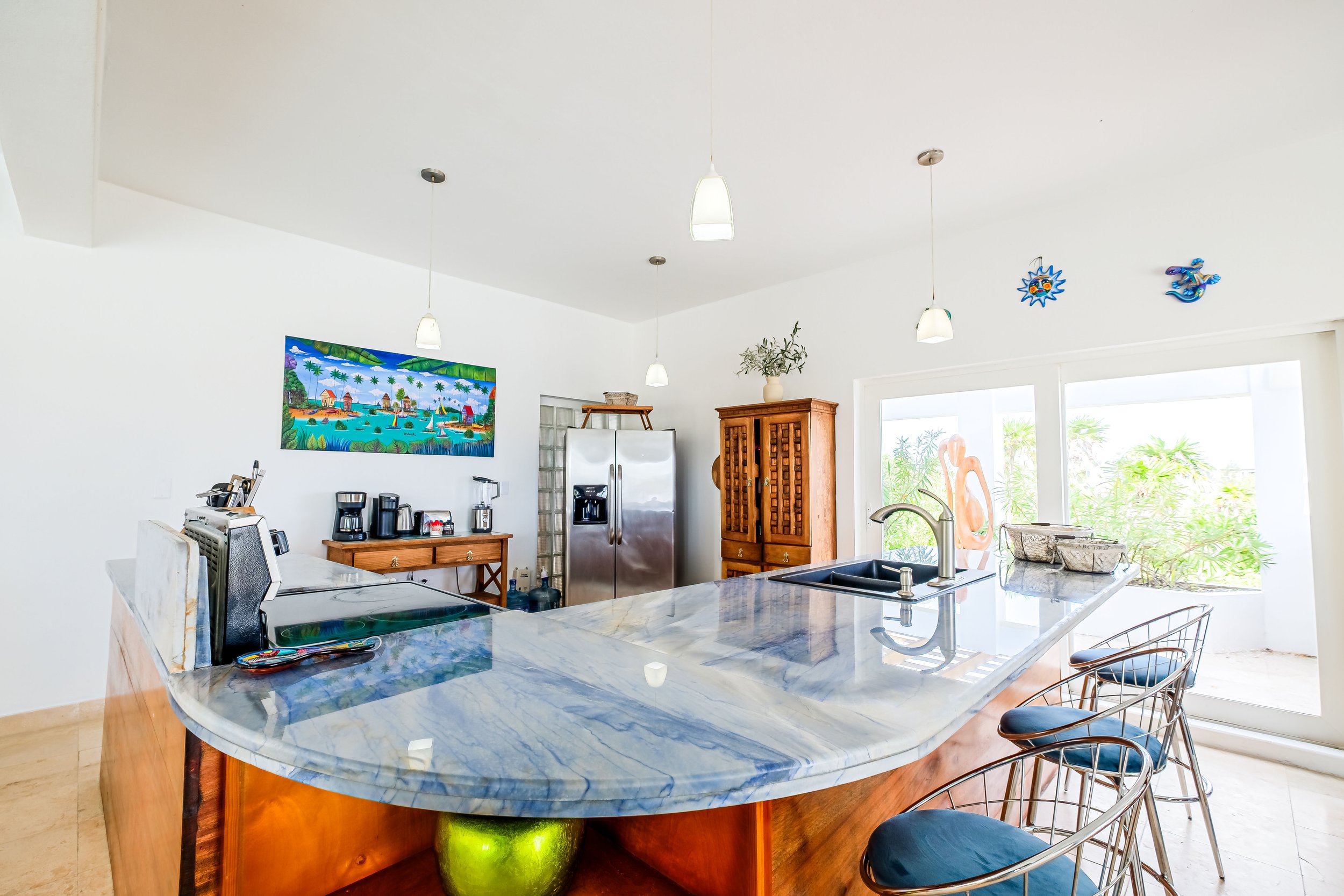 Modern kitchen with marble countertop, stainless steel appliances, wooden cabinets, and colorful wall art.