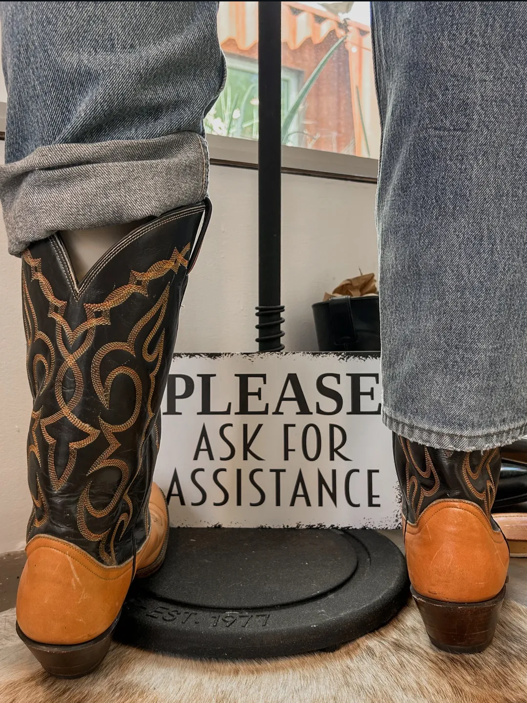 Vintage cowboy boots beside a “Please Ask for Assistance” sign inside ORTENSE.