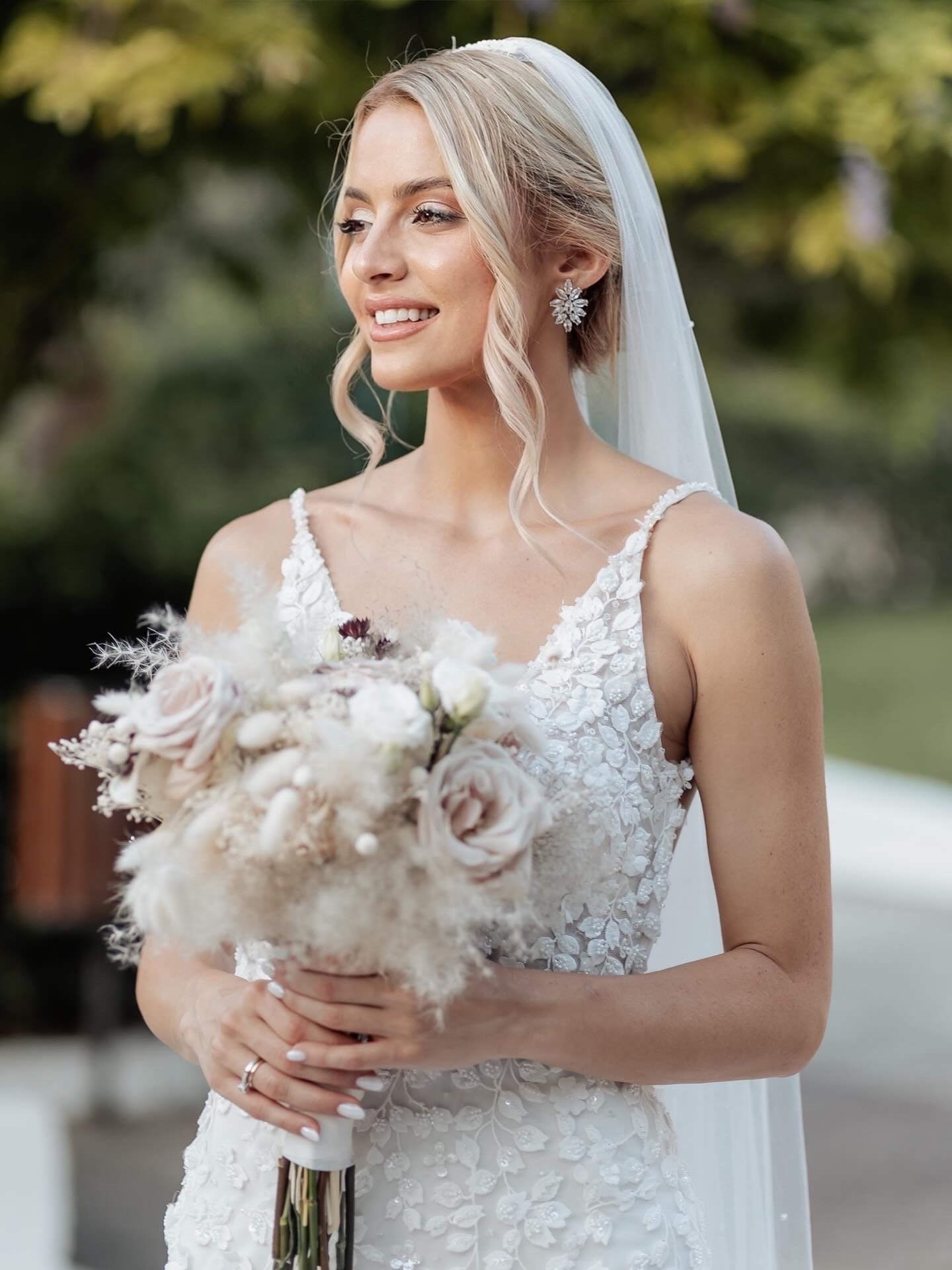 A bride in a white wedding dress holding a bouquet of flowers outdoors.