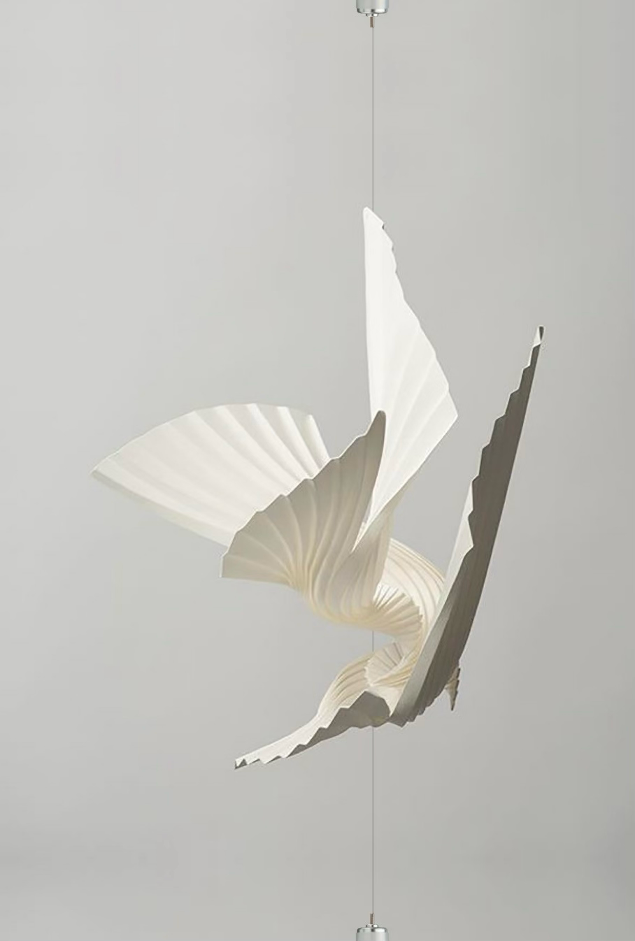 An abstract mobile sculpture consisting of white and gray paper shapes hanging from a thin wire, set against a plain light gray background.