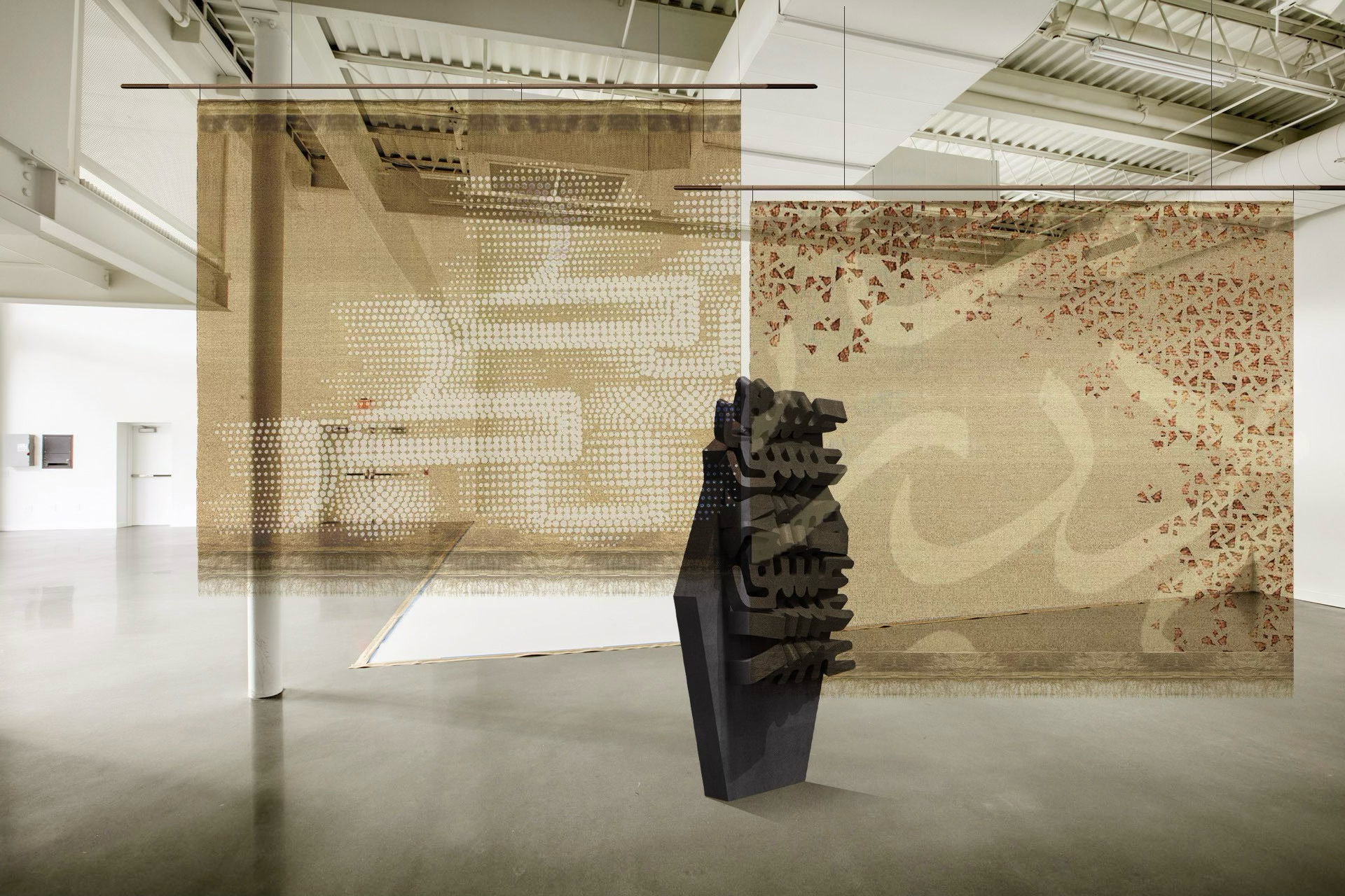 An art installation in a gallery featuring two large, semi-transparent hanging fabric panels with abstract patterns, and a dark sculptural piece shaped like a stack of faces in front of the right panel.
