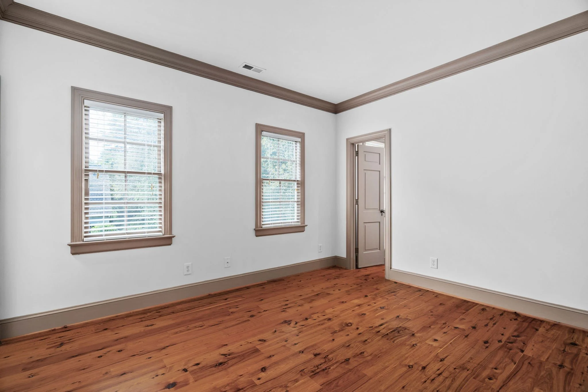 Empty room with white walls, hardwood floor, three windows with blinds, and a closed door.