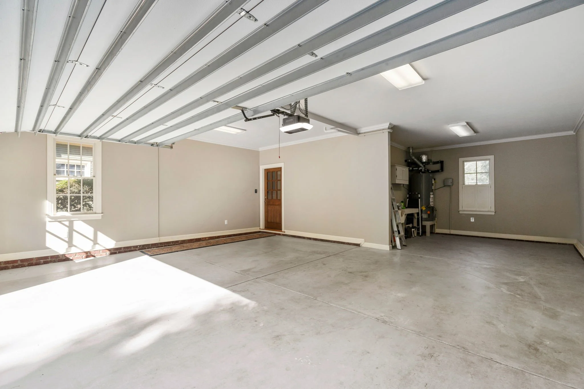Empty two-car garage with concrete floor, gray walls, two windows, and an open garage door.