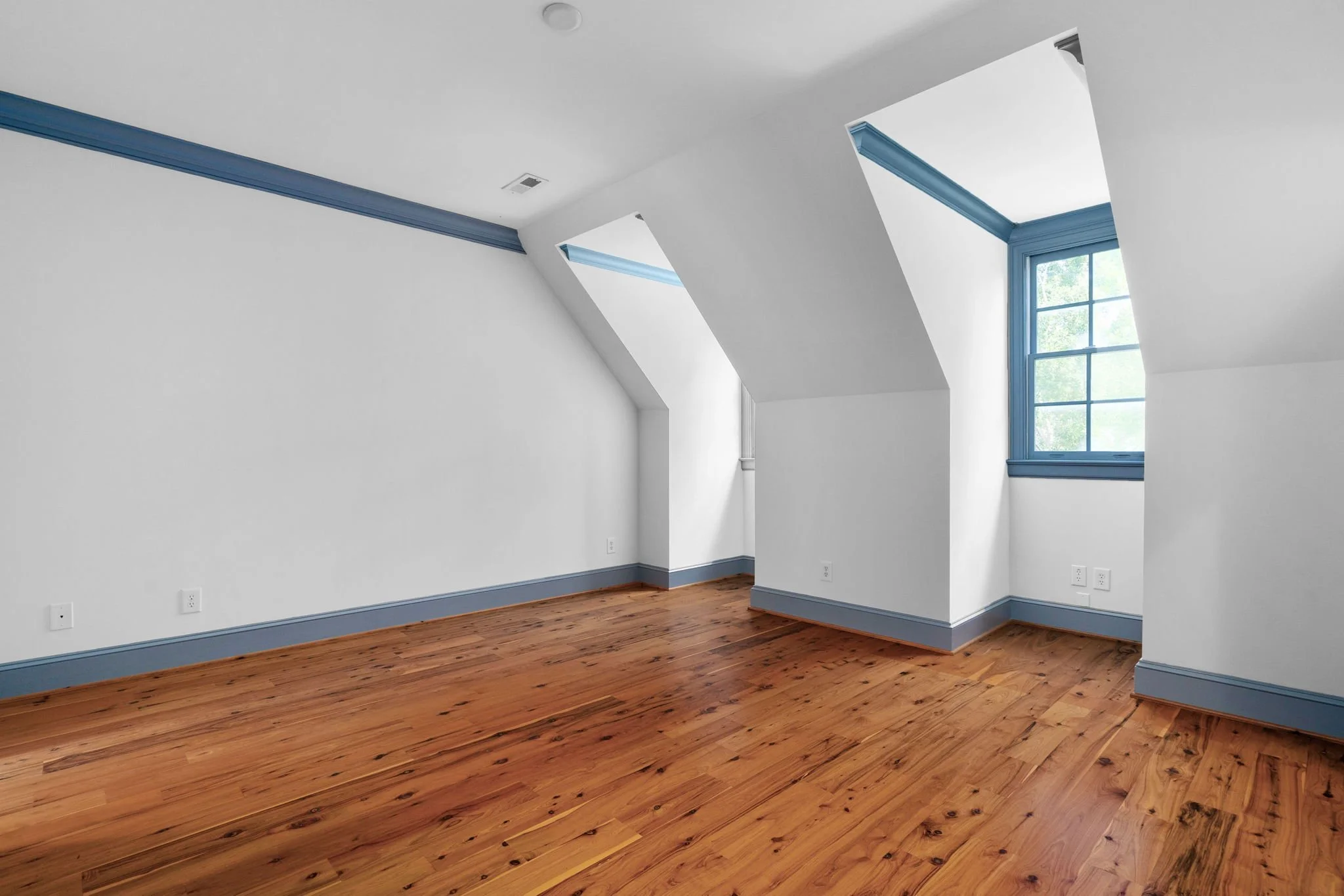 Empty room with white walls, blue trim, hardwood flooring, and windows with blue frames.