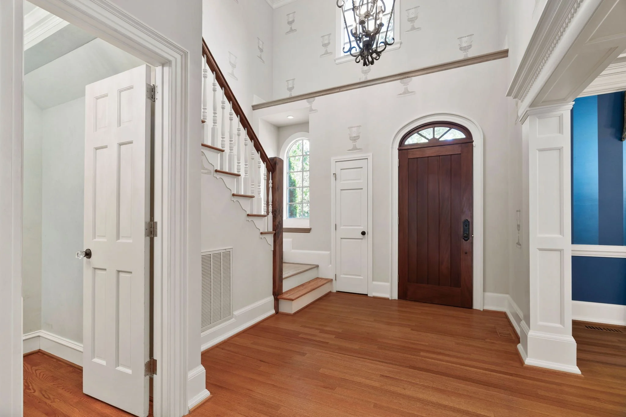 Entryway with wooden front door, staircase with white balusters, hardwood floor, and white walls with decorative molding.