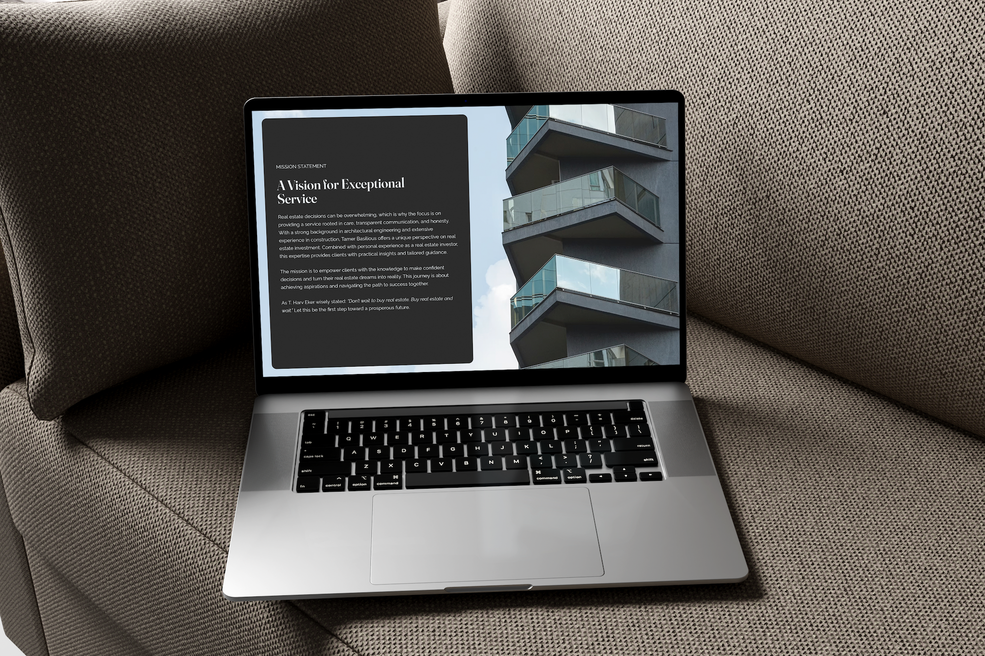 A laptop sitting on a brown fabric couch, displaying a webpage with a black background and white text about real estate service, with a photo of a modern building with glass balconies on the right side of the screen.