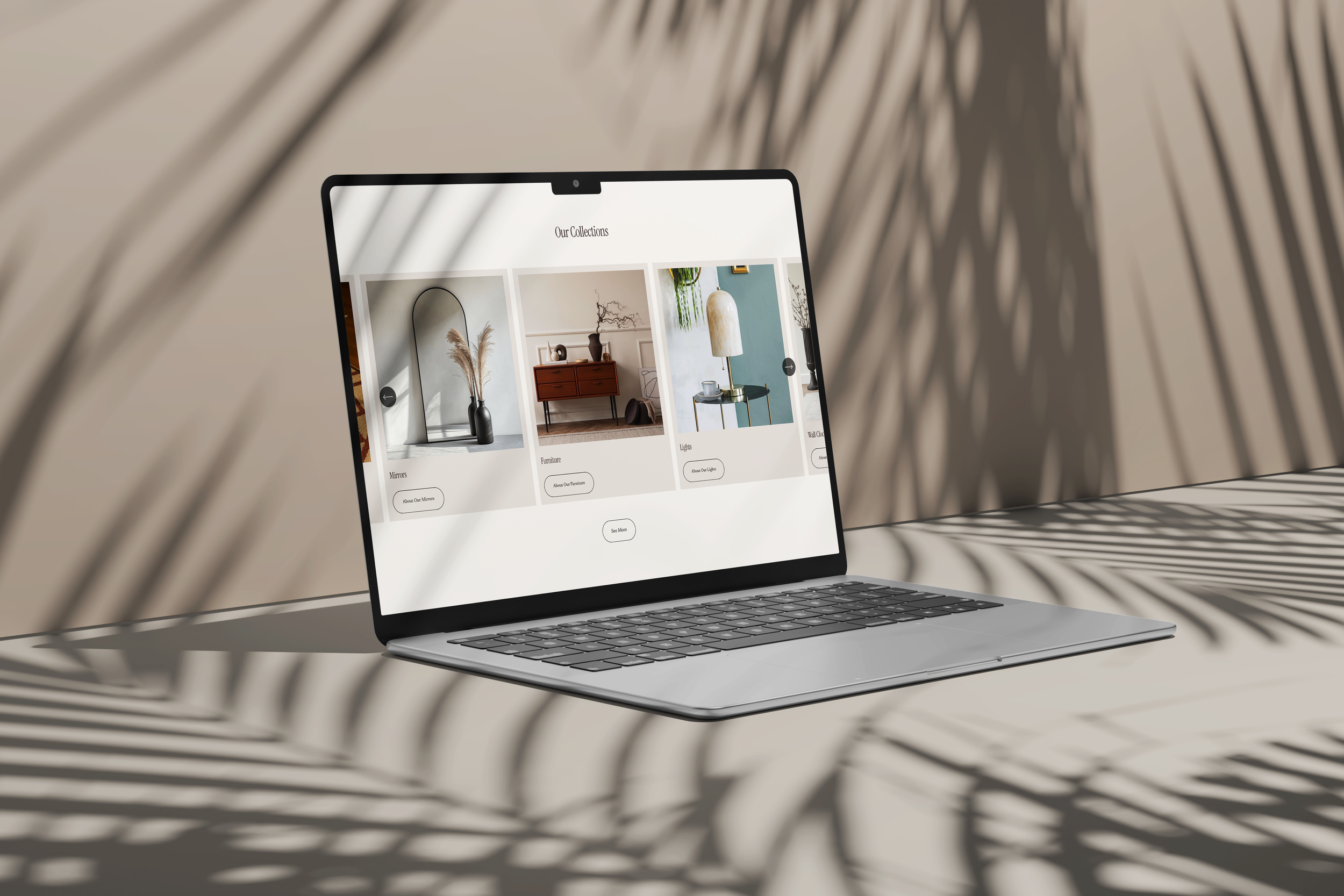A laptop on a table displaying an interior decor website with home furnishings and accessories, with shadows of palm leaves cast across the scene.