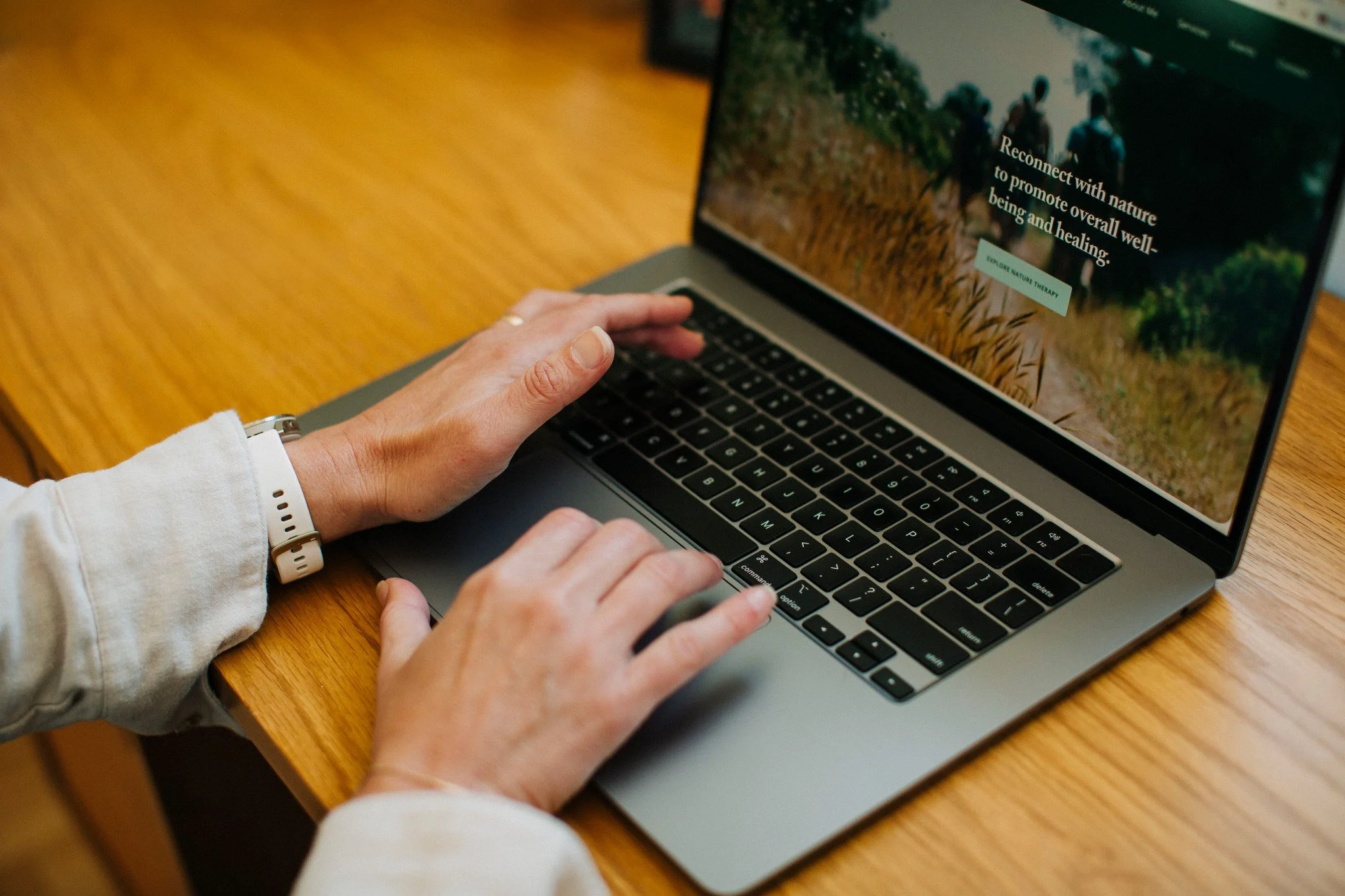 Nana Potenza using a laptop with a nature-themed website open, sitting at a wooden table.