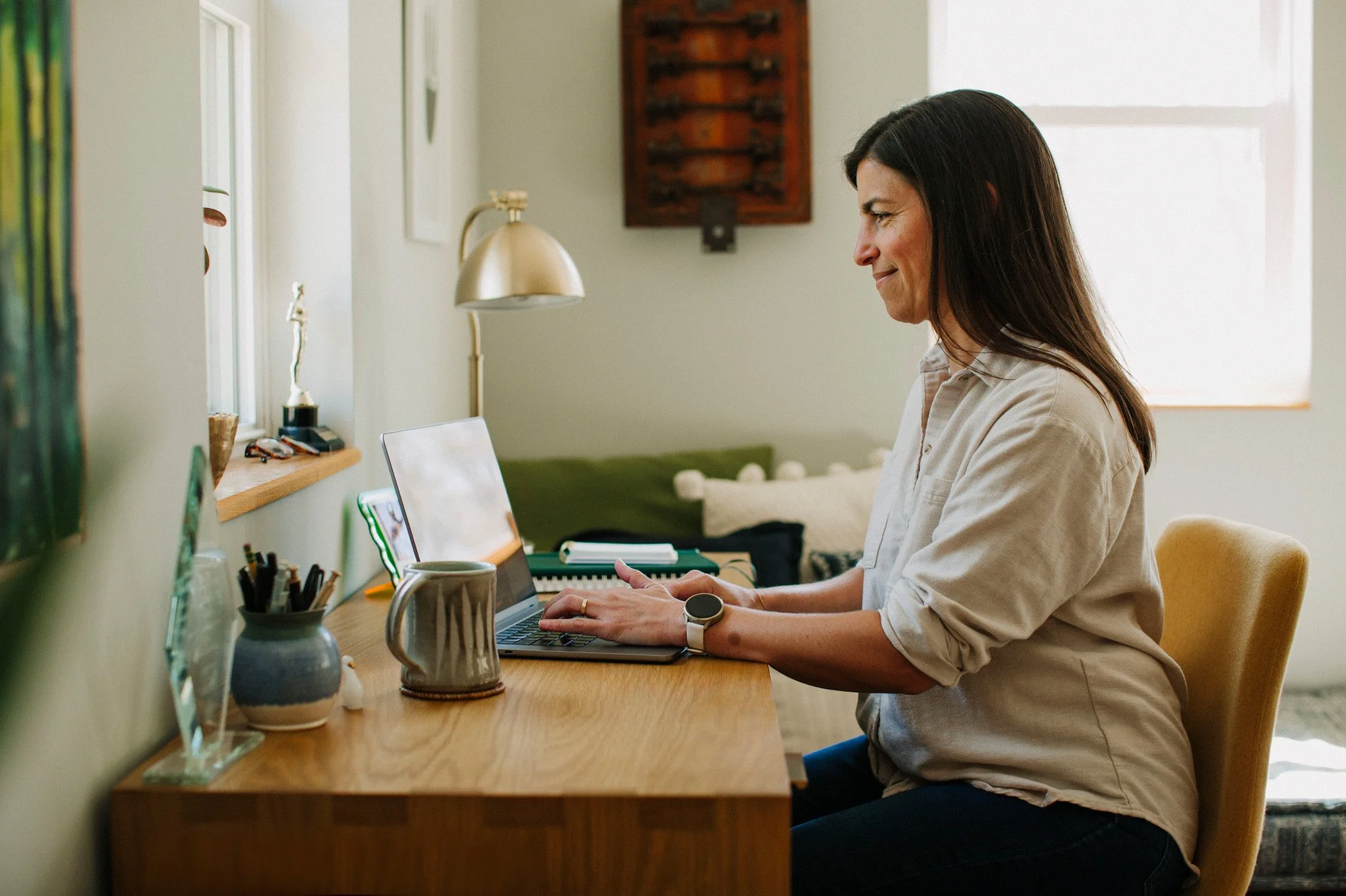 Nana working on a laptop at a wooden desk in a brightly lit cozy room.