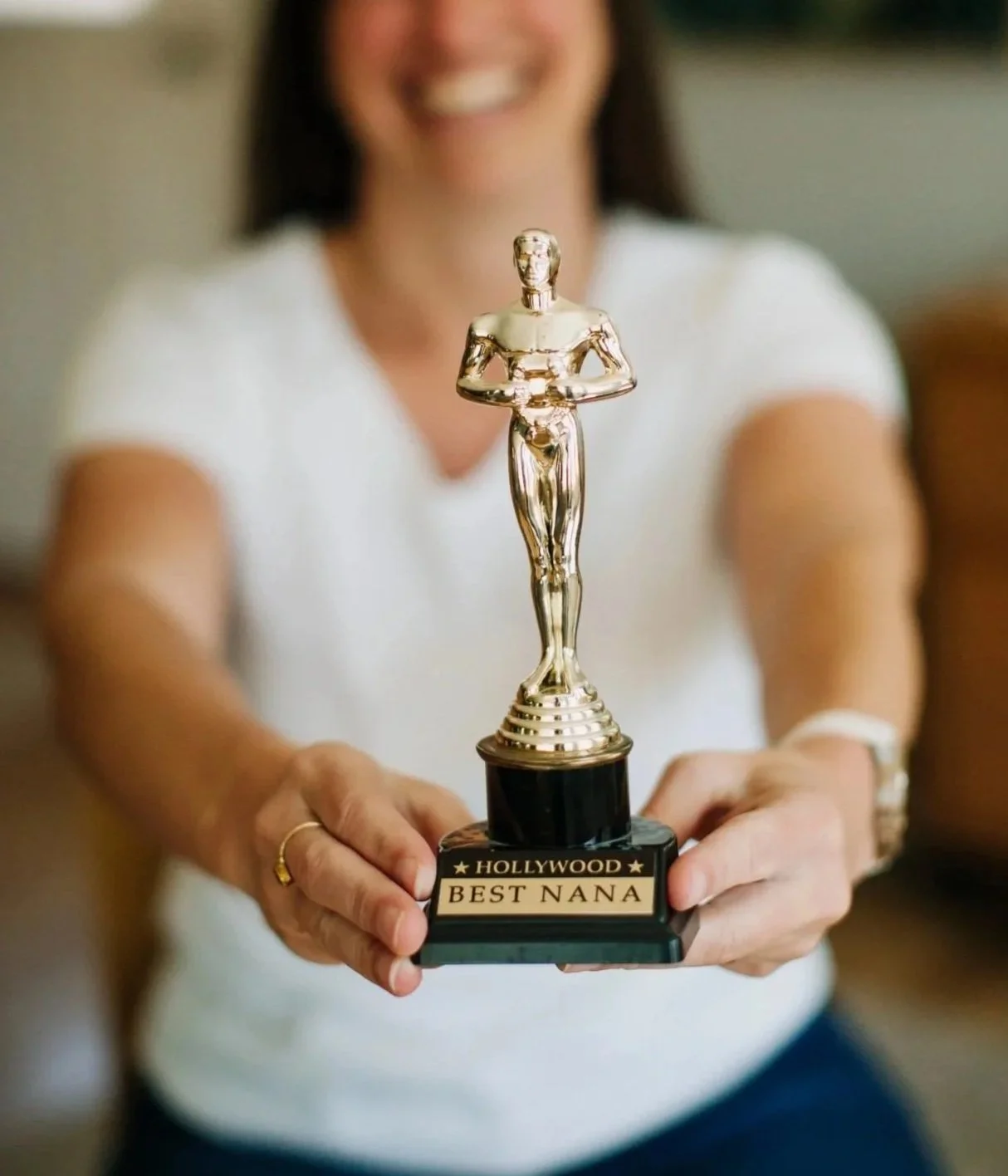 Nana in a white t-shirt holding a trophy with a gold-colored statuette, labeled "Hollywood Best Nana."
