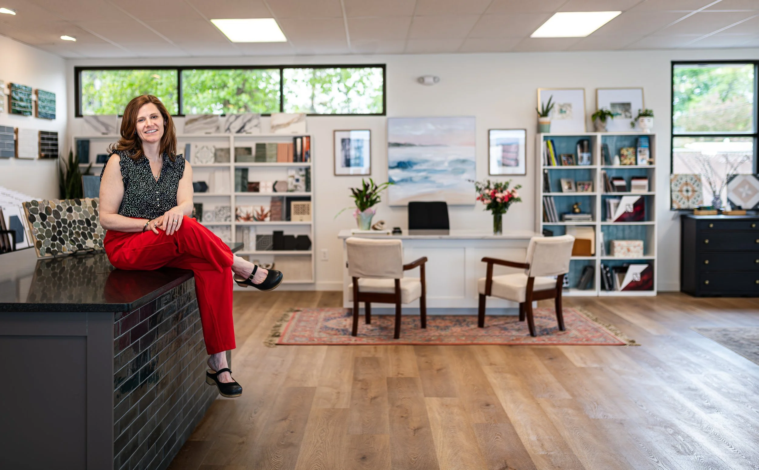 Kelly Strawbridge-Dixon, owner of Red Bird Tile, sitting on her desk in her tile showroom, smiling at the camera.