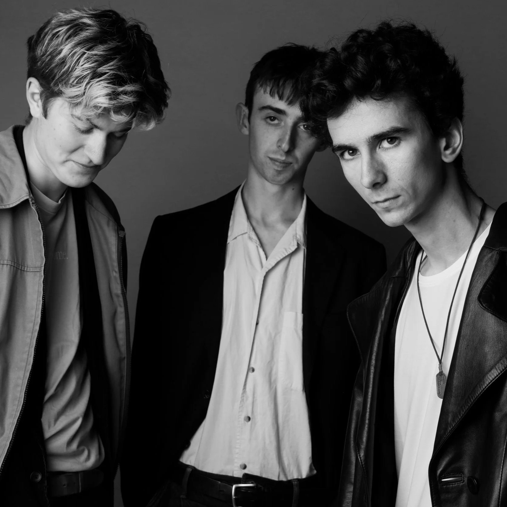 Black and white photo of three young men with serious expressions, standing close together against a plain background.
