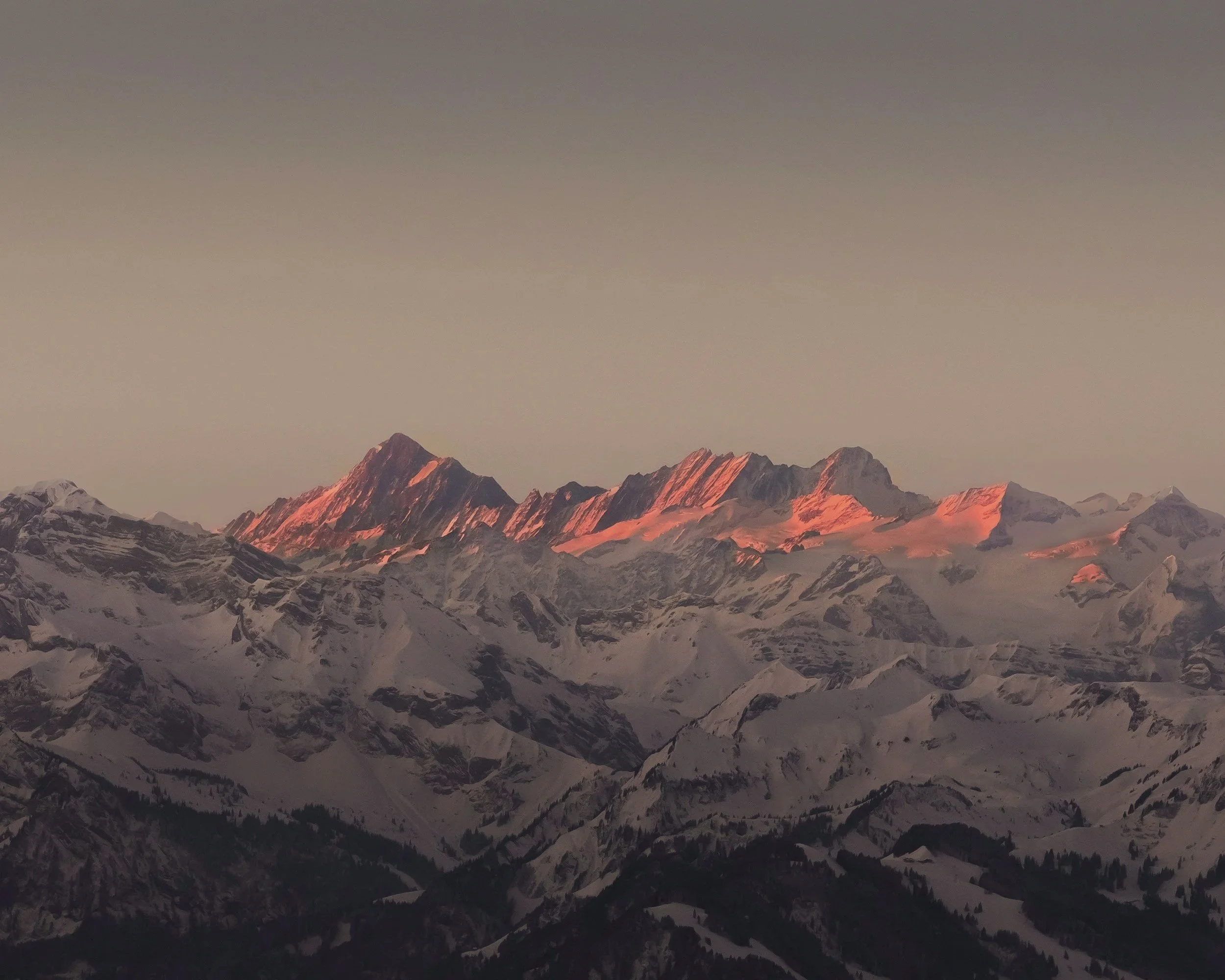 Snow-covered mountain range at sunset with peaks illuminated in pink and orange hues.