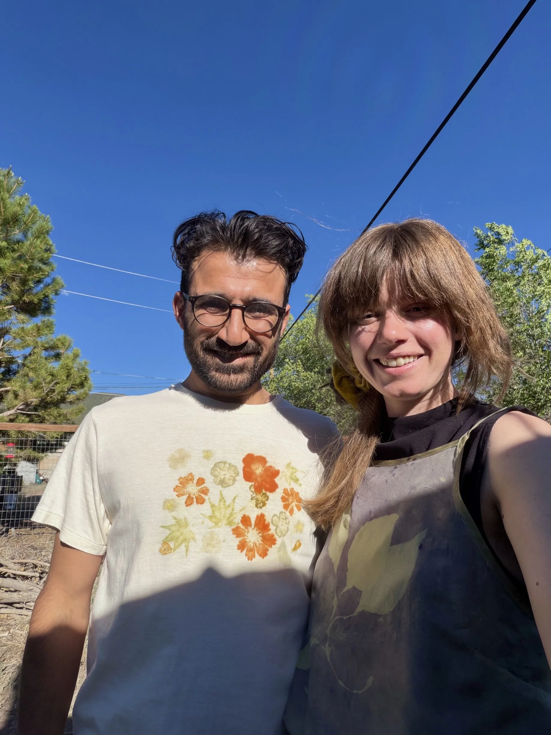A man and woman taking a selfie outdoors on a sunny day, smiling with trees and a clear blue sky in the background wearing naturally dyed clothing naturally dyed clothing naturally dyed clothing naturally dyed clothing naturally dyed clothing