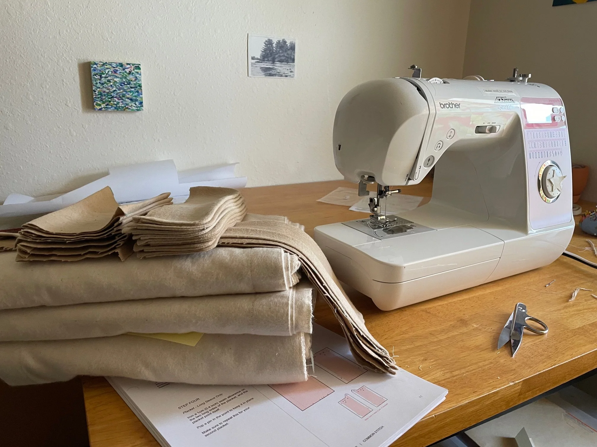 A sewing machine and stacks of fabric that will become the Gingko Flannel on a wooden desk, with sewing pattern instructions and scissors nearby.