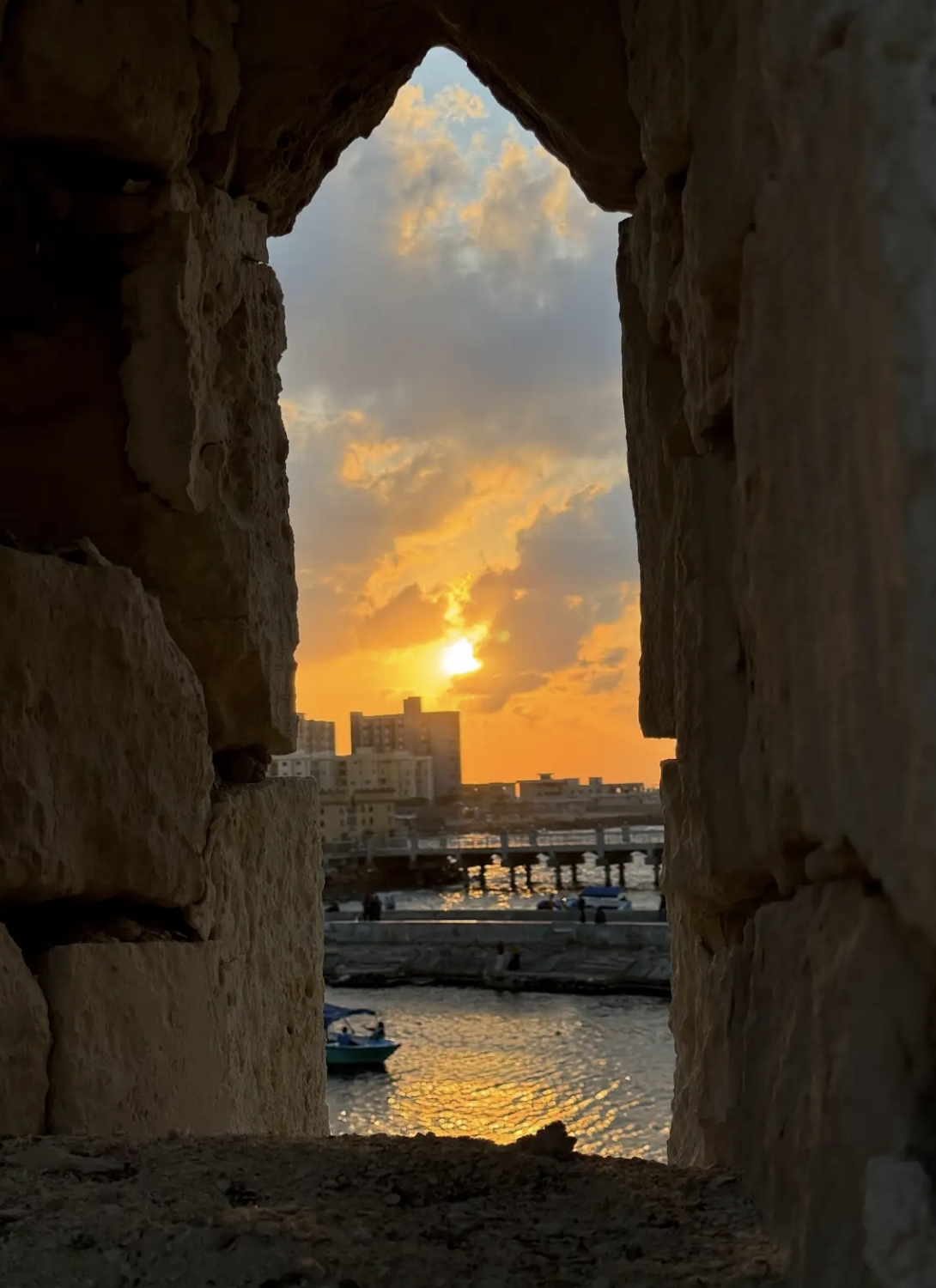 View of a harbor at sunset through a stone window in an old building.