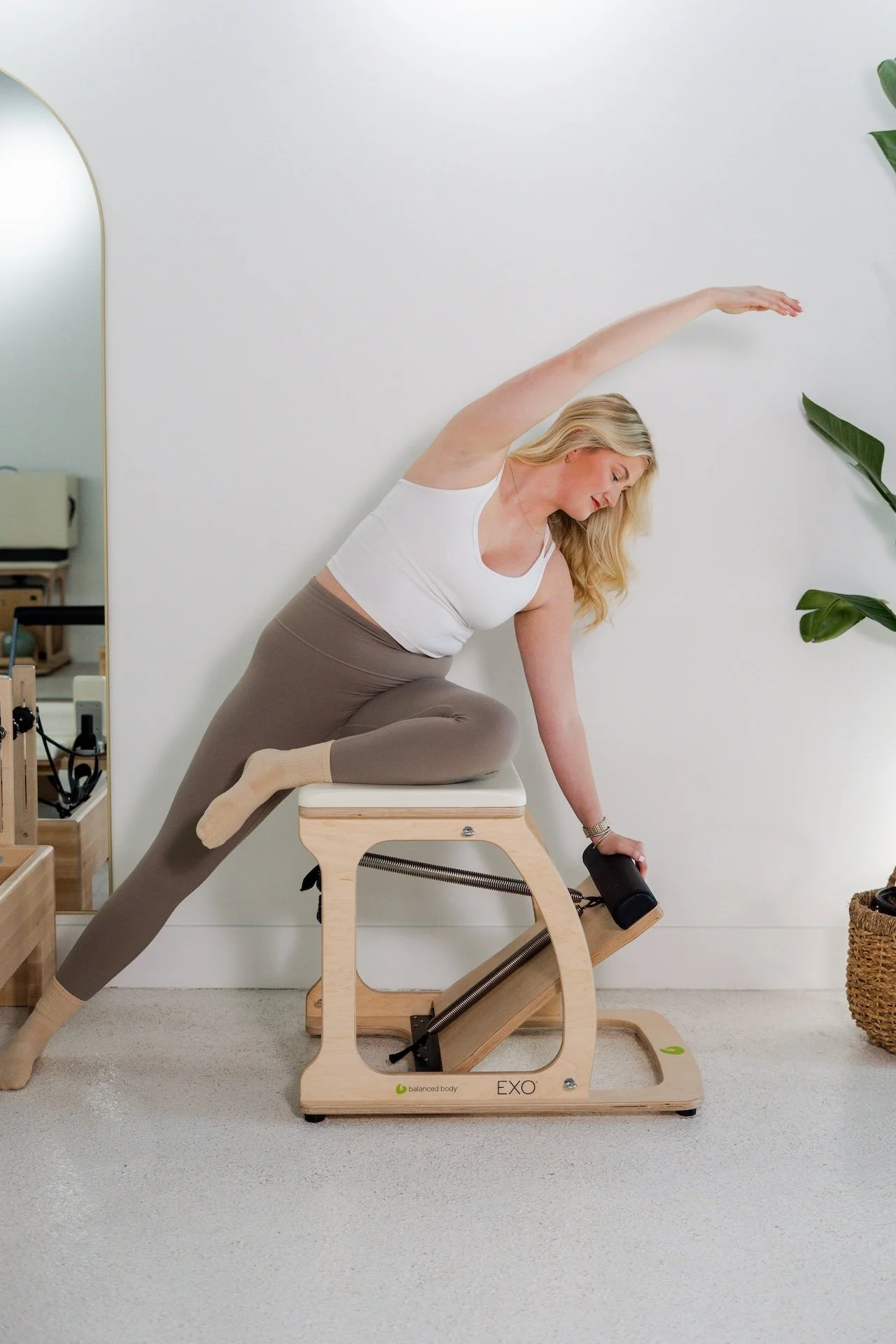 Two women exercising in a Pilates studio using fitness equipment, with one woman wearing a black shirt and both wearing black leggings.