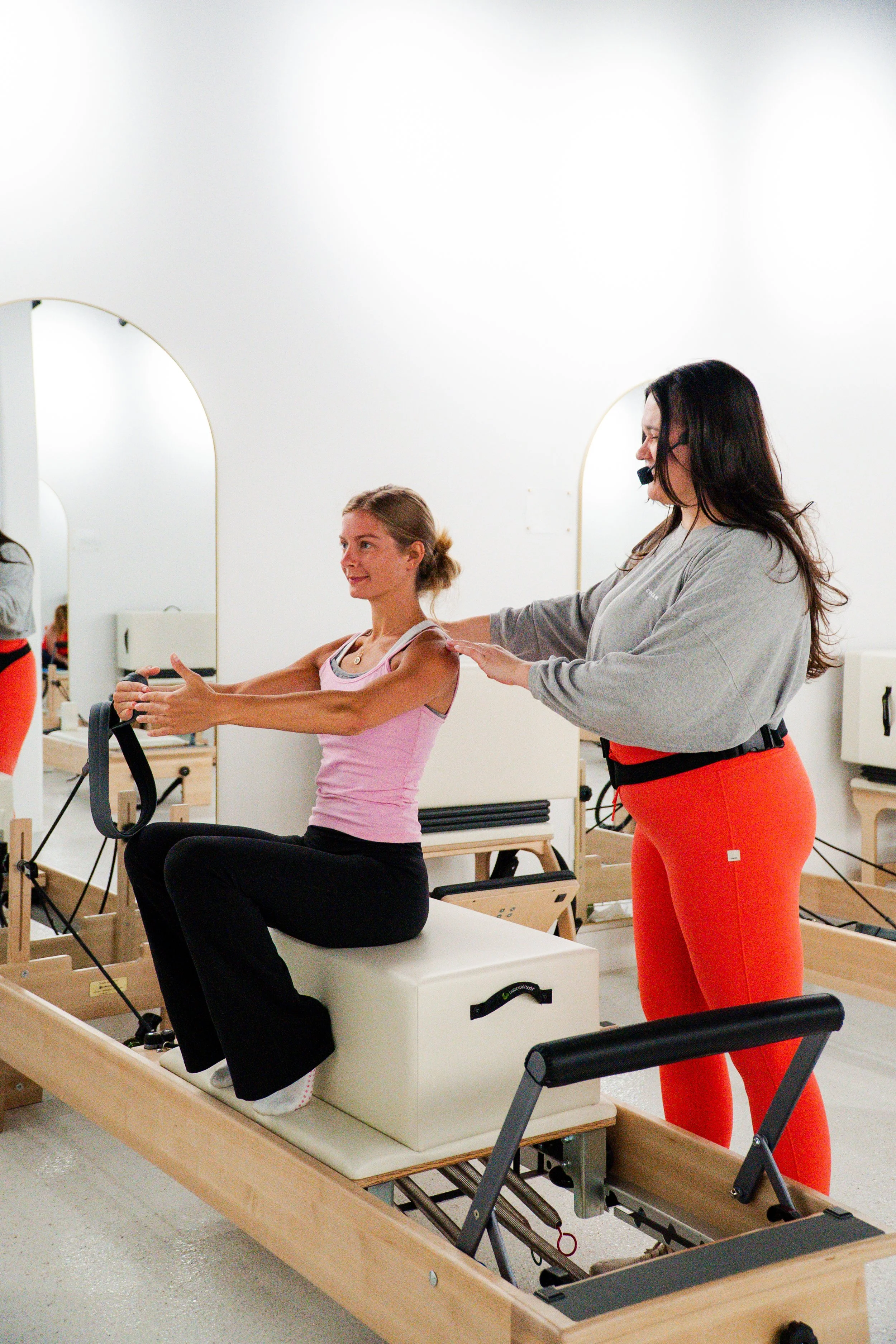 Person doing a Pilates exercise on a reformer with a small exercise ball behind their knee.