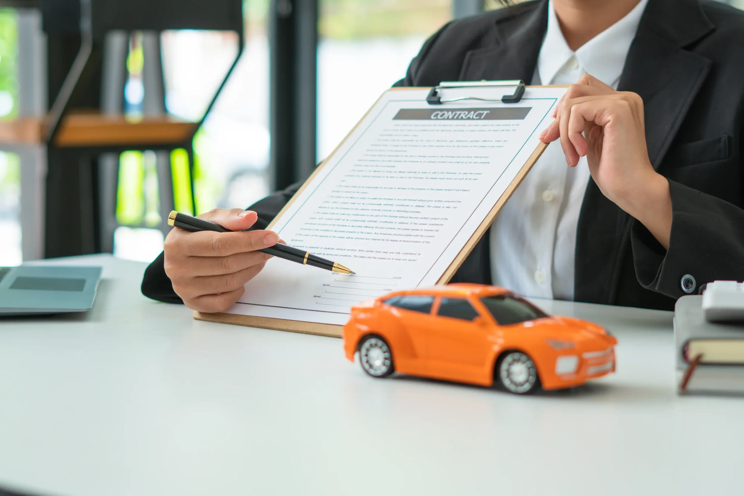 Asesor muestra contrato junto a un auto de juguete para el cambio de propietario de vehículo de forma segura.
