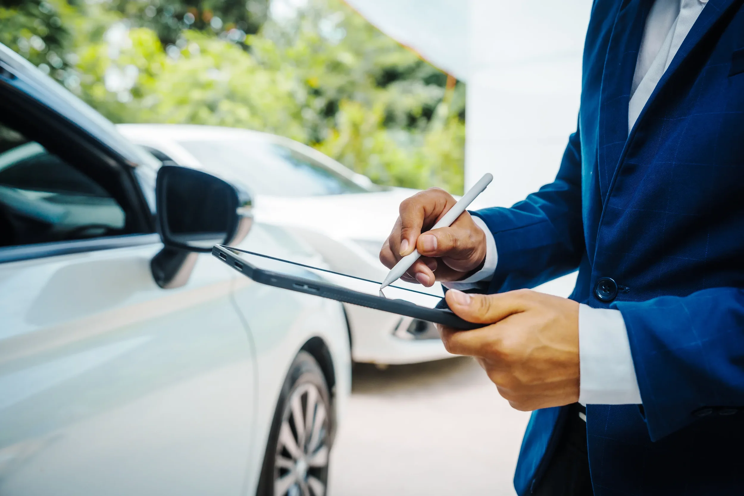 Asesor en traje usa tableta para revisar un auto antes de validar el cambio de propietario de vehículo en la oficina.
