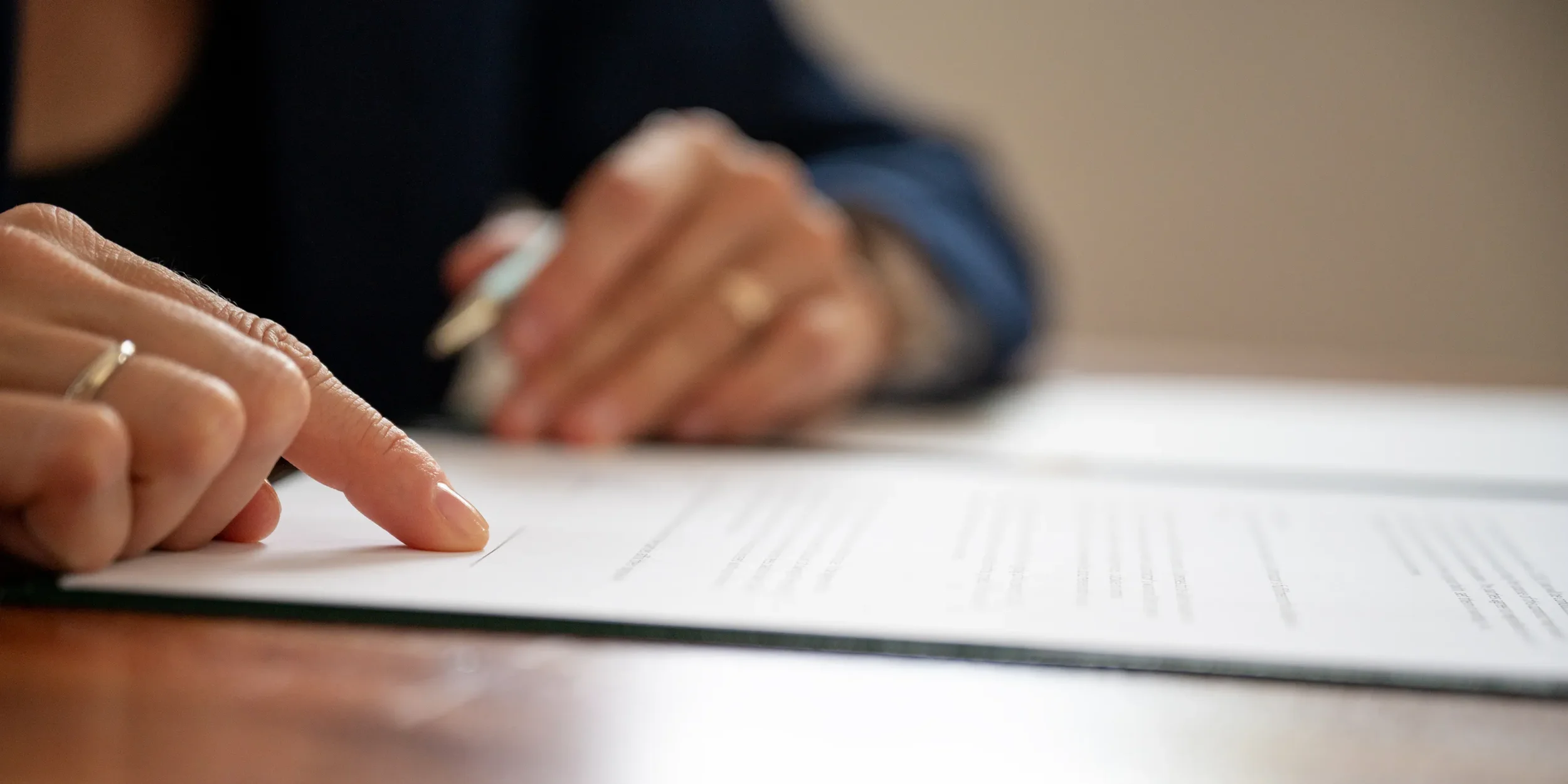 Persona indicando con el dedo dónde firmar el contrato definitivo para completar el alta de vehículo sobre un escritorio
