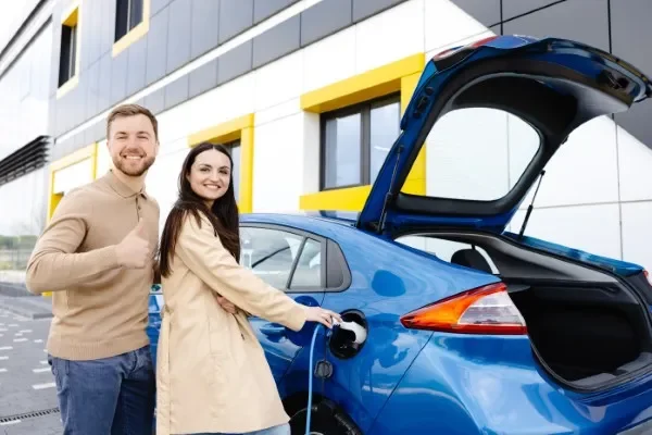Pareja feliz cargando su coche azul gracias a la instalación de cargadores eléctricos para autos de alta velocidad.