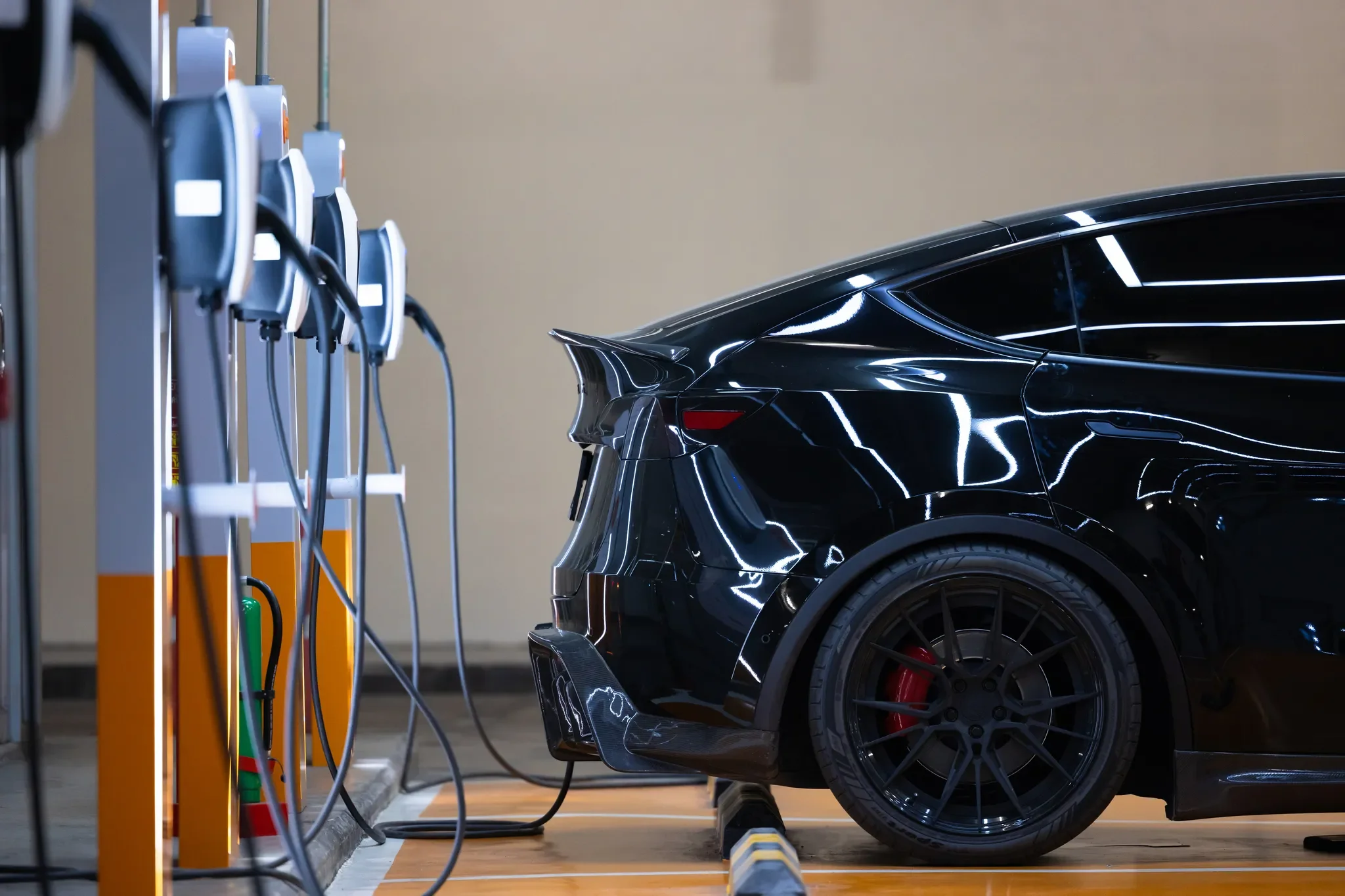 Vista trasera de un auto eléctrico más barato de color negro estacionado frente a una serie de cargadores de pared modernos.