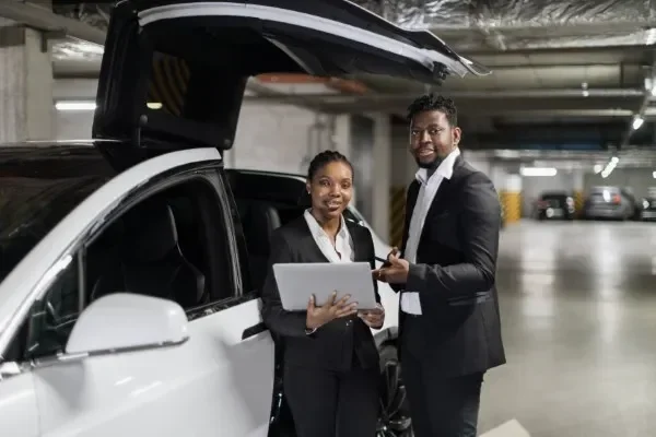 Especialistas en gestoría vehicular empresarial revisando plataformas digitales junto a un automóvil de la flota.