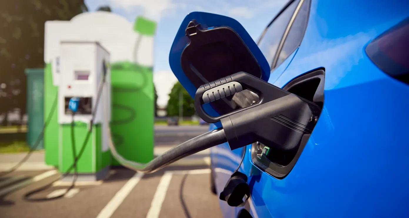 Detalle de manguera conectada a un auto eléctrico más barato cargando batería en una estación de servicio pública verde.