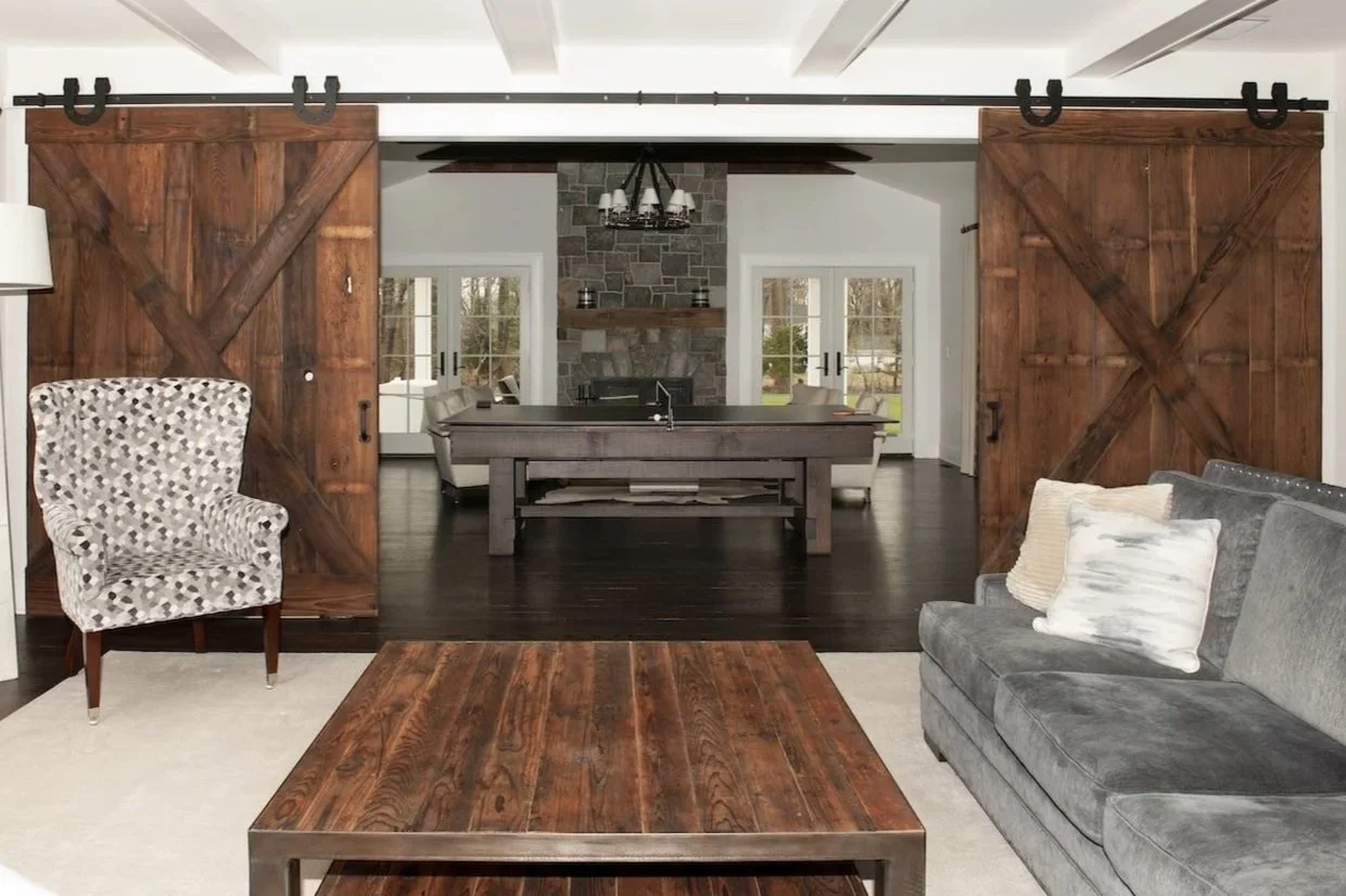 Home with a reclaimed barnwood coffee table, large reclaimed wood barn doors opening onto a game room with faux beams and a reclaimed beam mantel.