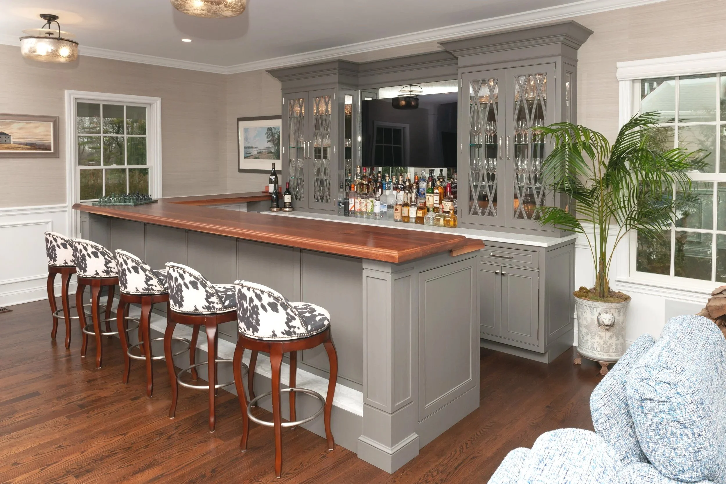 Home bar with a black walnut bar top on gray cabinets with walnut stools.