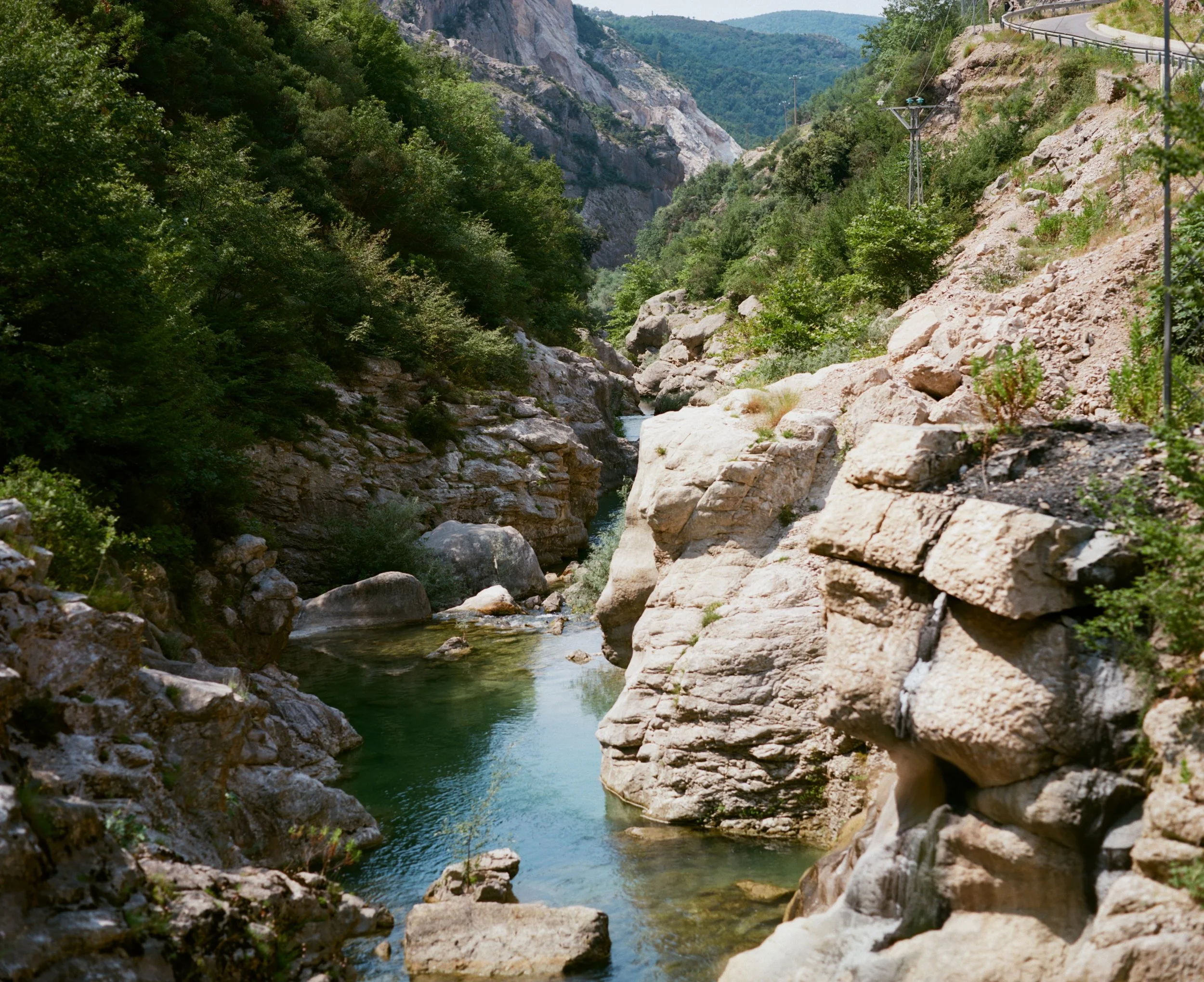 A rocky canyon with a narrow, winding river flowing through it, surrounded by green trees and steep, rugged cliffs.