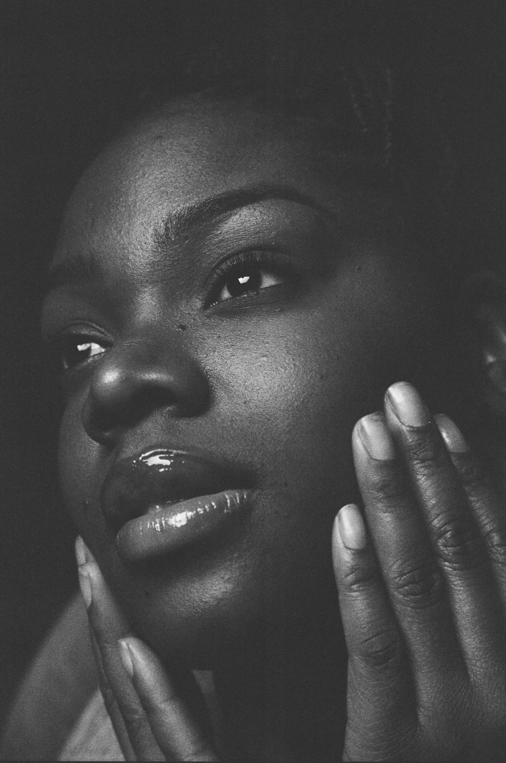 Close-up black and white photograph of a woman's face, showing her eyes, nose, and lips, with one hand gently touching her cheek.