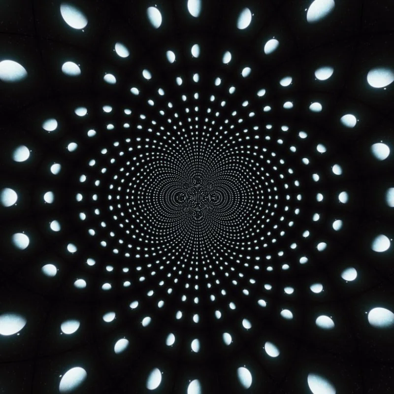 A tunnel with a spiral pattern of evenly spaced circular holes letting light through, creating an illusion of a deep, endless vortex.