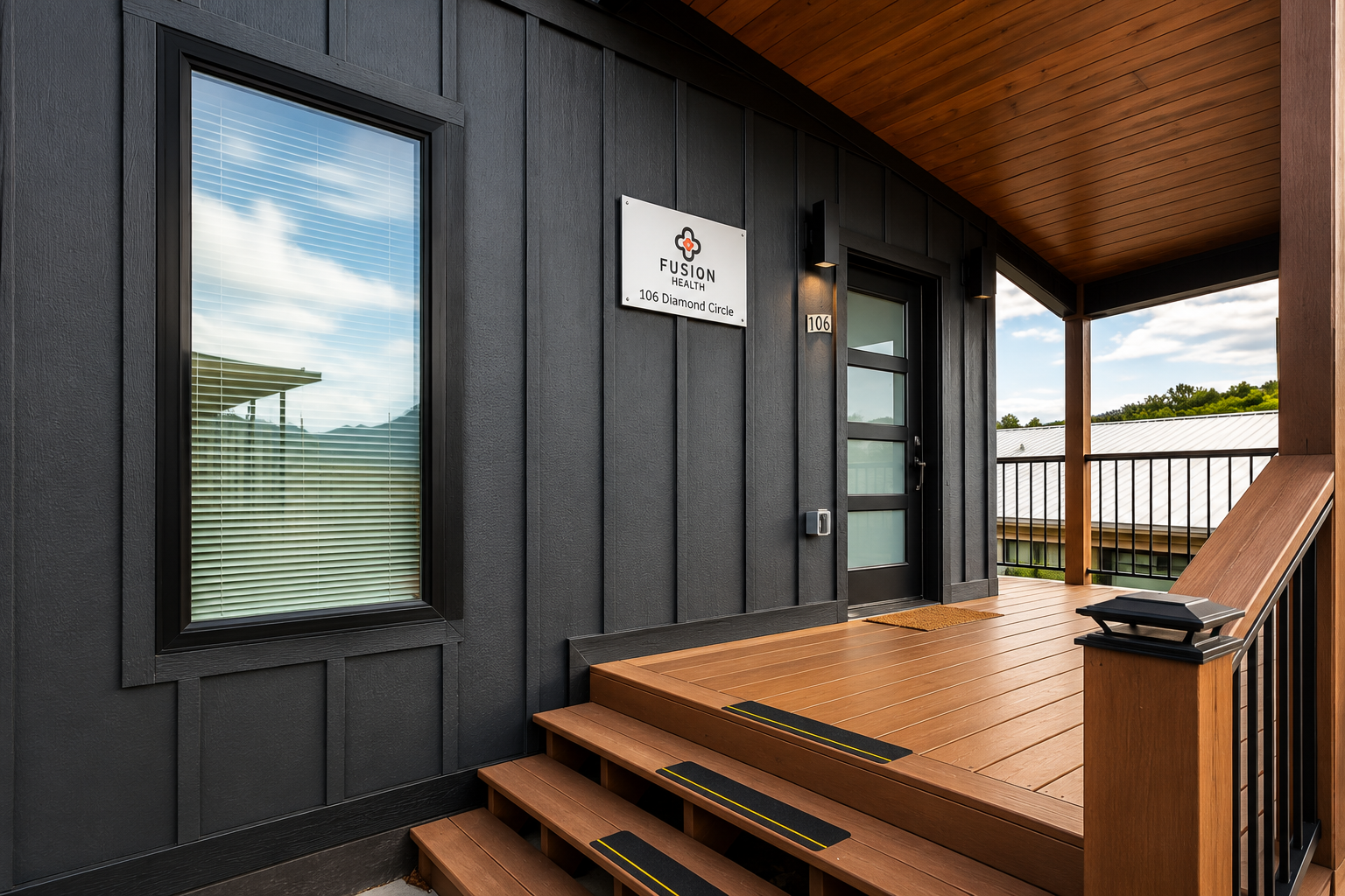 Front porch of a modern black and wood-paneled building with a window, door, and a sign that reads 'Fusion Health 106 Diamond Circle' in a suburban area.