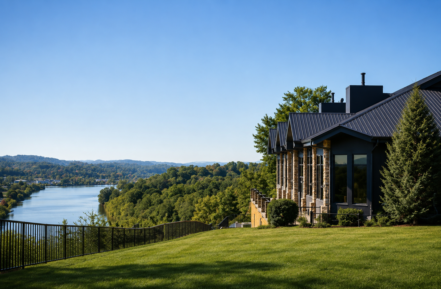Contemporary house with large windows and black metal roof overlooking a river and lush green landscape.