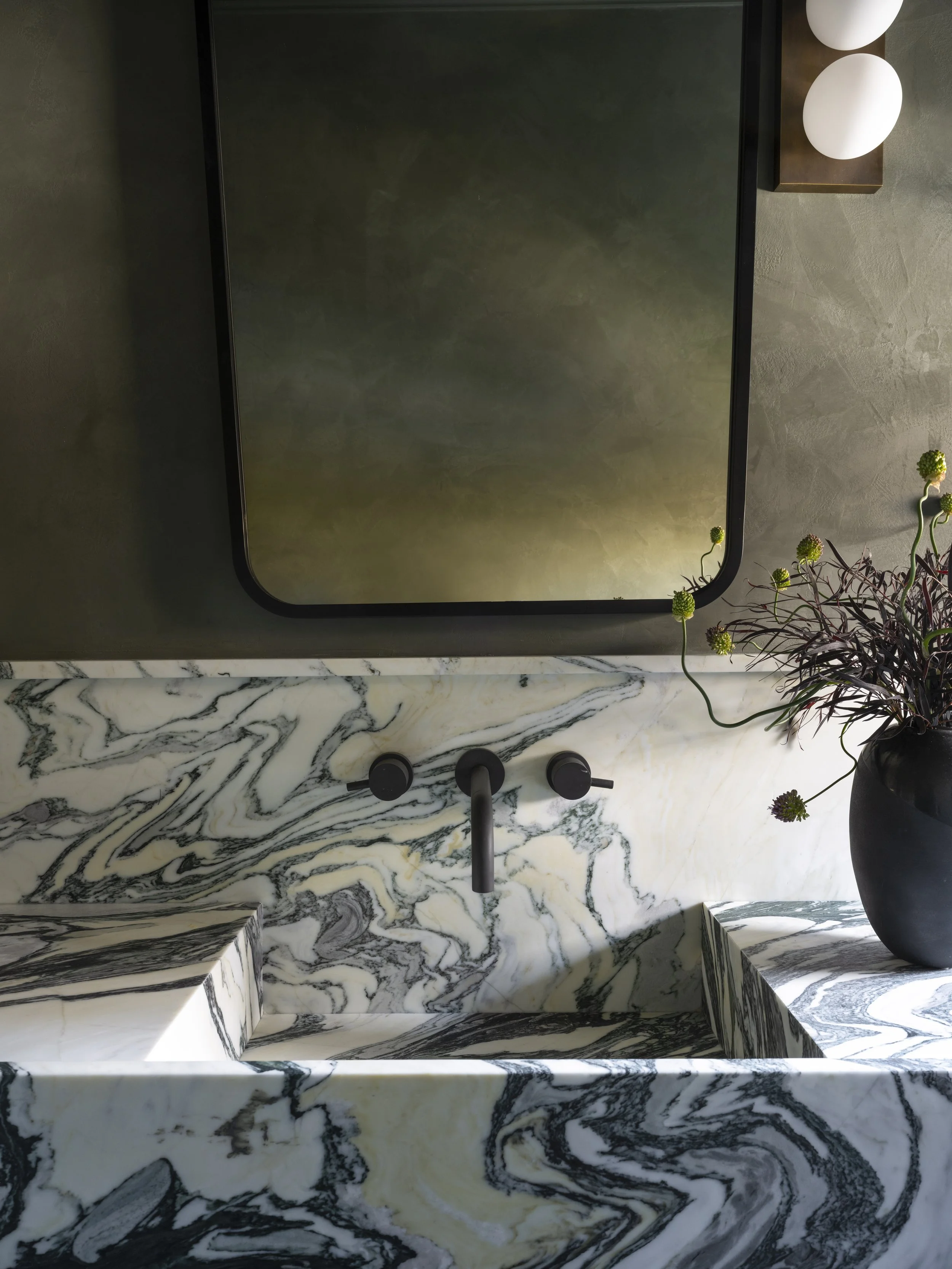 Dramatic Calacatta marble vanity featuring bold organic veining, moody plaster walls, matte black fixtures, and sculptural contemporary detailing with art-driven styling