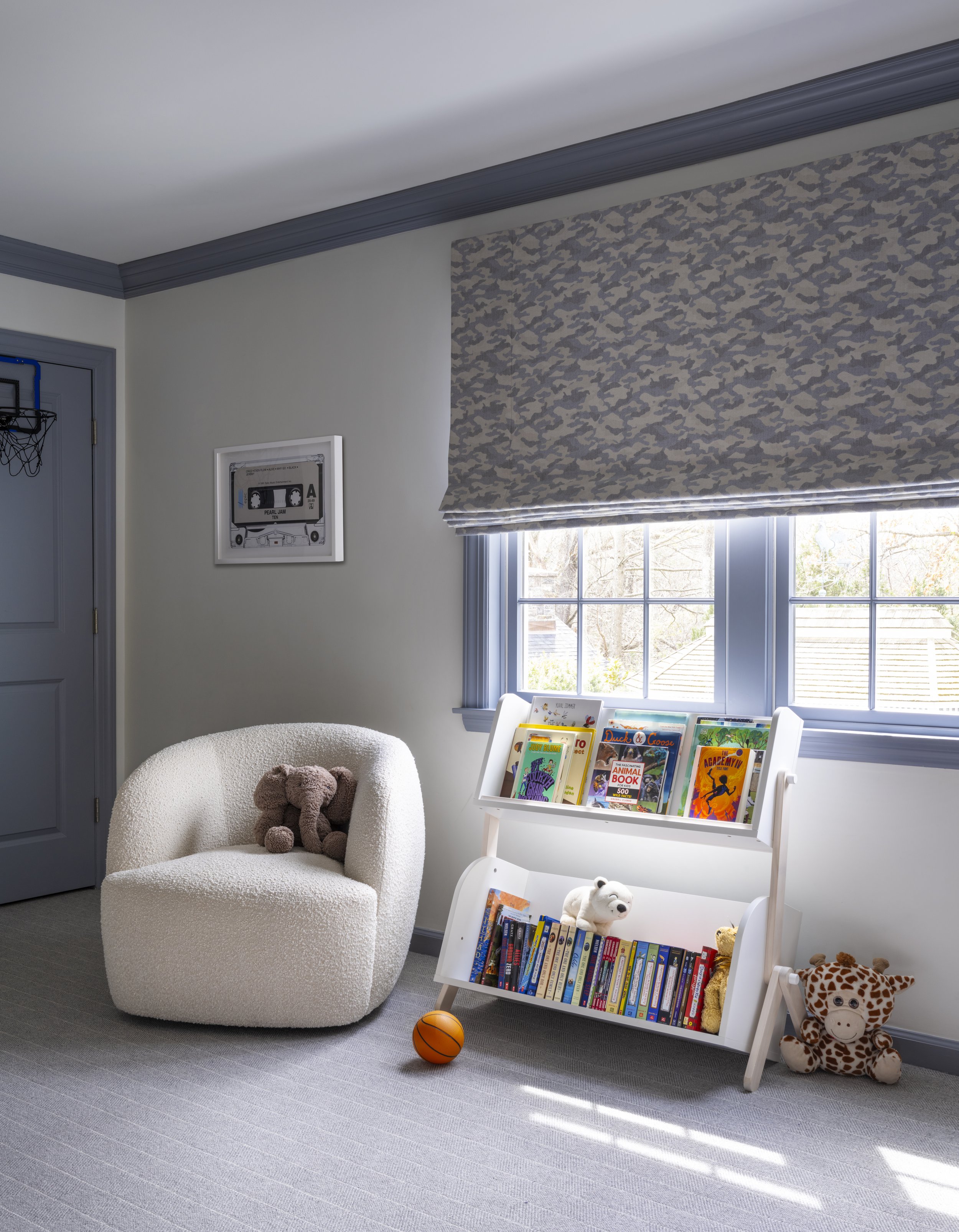 Refined children’s reading nook featuring sculptural boucle seating, tailored Roman shades, and curated book display styling with soft contemporary detailing and playful family-focused design