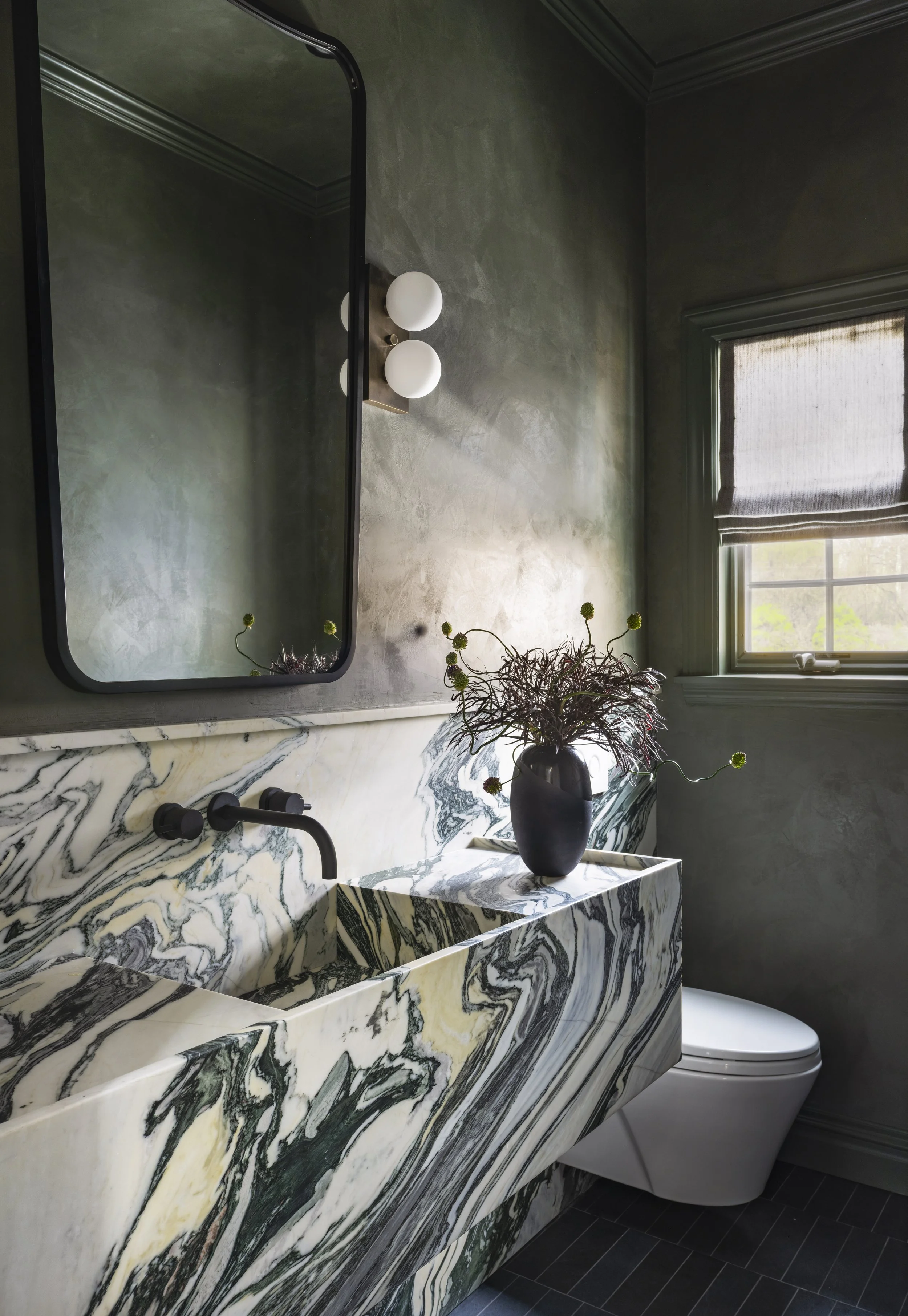 Dramatic contemporary powder room featuring a sculptural Calacatta marble vanity, moody limewash walls, matte black fixtures, and gallery-inspired styling with richly layered architectural character