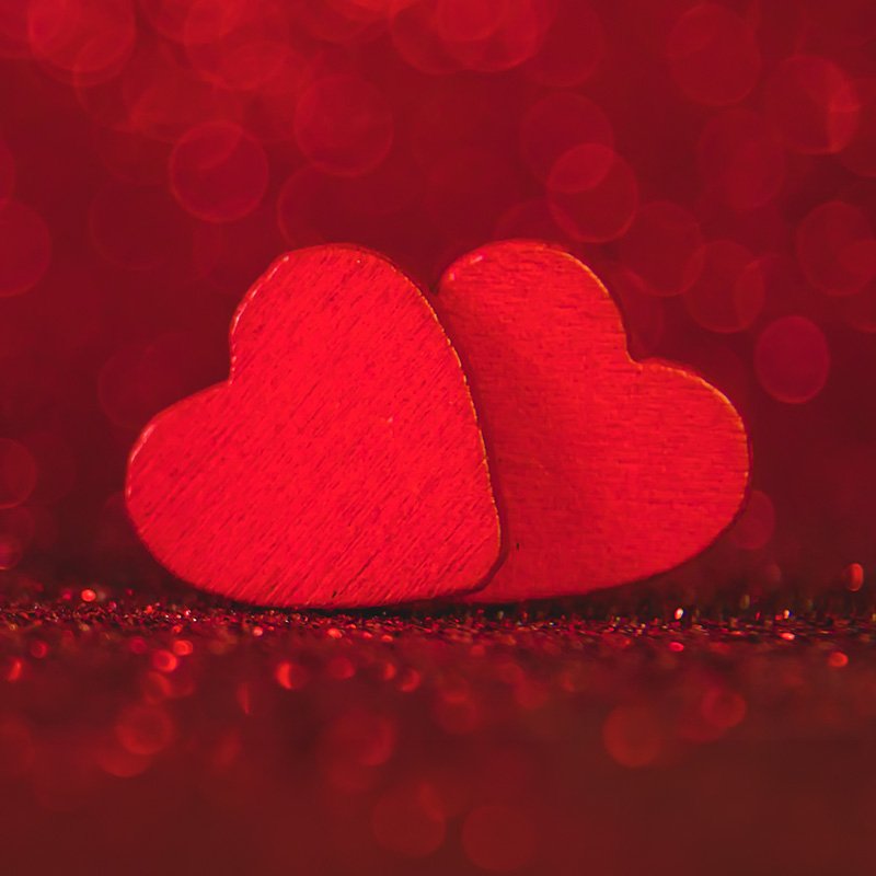 Two pink paper hearts overlapping on a black background.