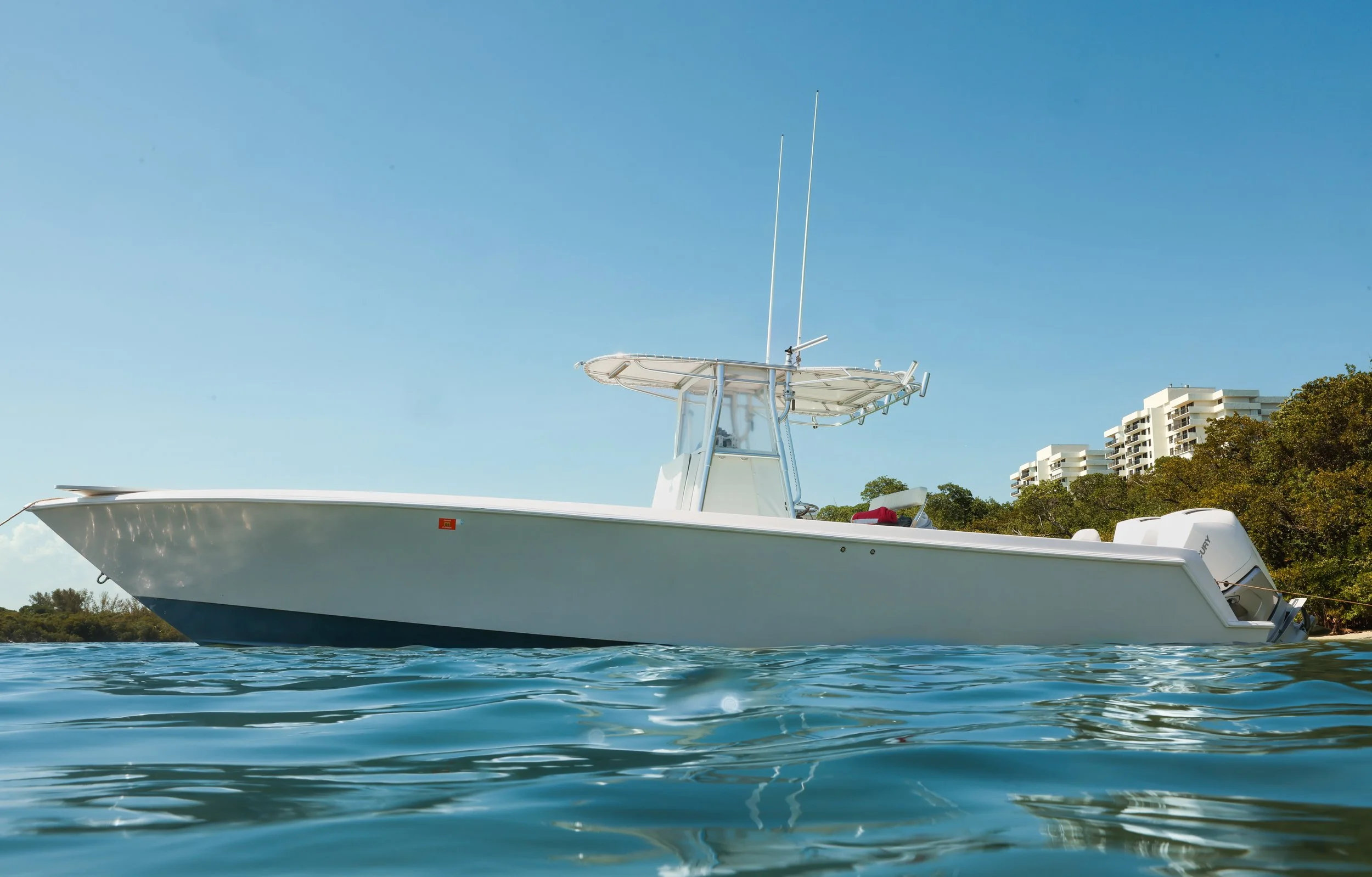 A white motorboat floating on calm blue water with a clear sky and buildings in the background.