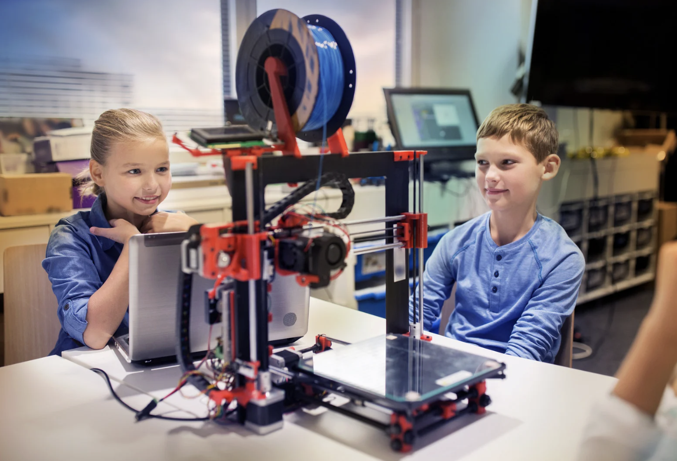 Two students sit in front of a 3D printer