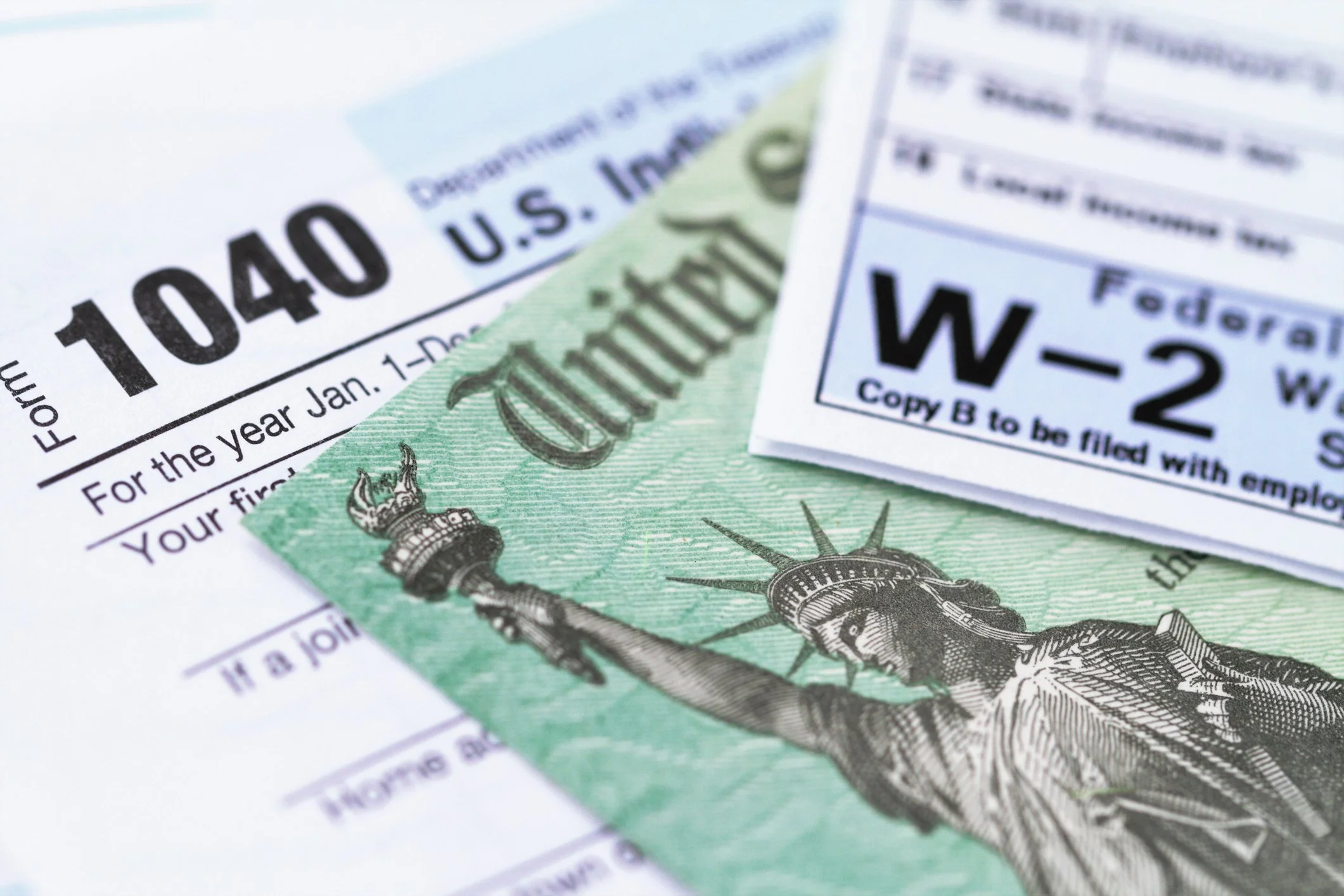 Close-up of U.S. tax documents including Form 1040, W-2, and a government issued check featuring the Statue of Liberty image.