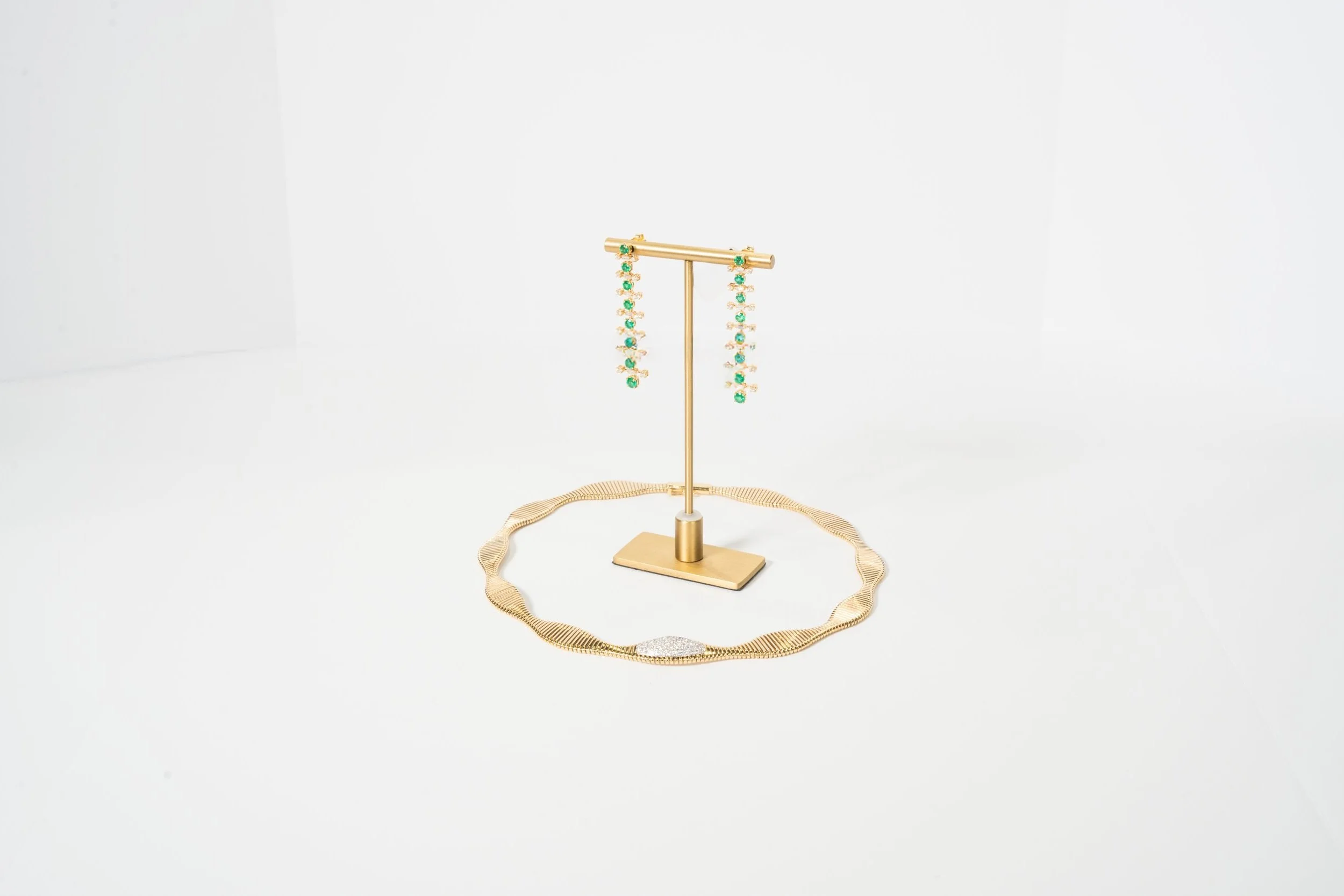 Emerald dangly earrings on display along with a gold and diamond necklace