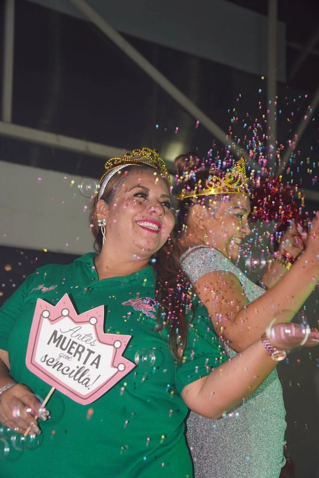 Mujeres festejando, una de ellas con corona y un cartel que dice 'Antes MUERTO que sencilla', rodeadas de confeti en una celebración.