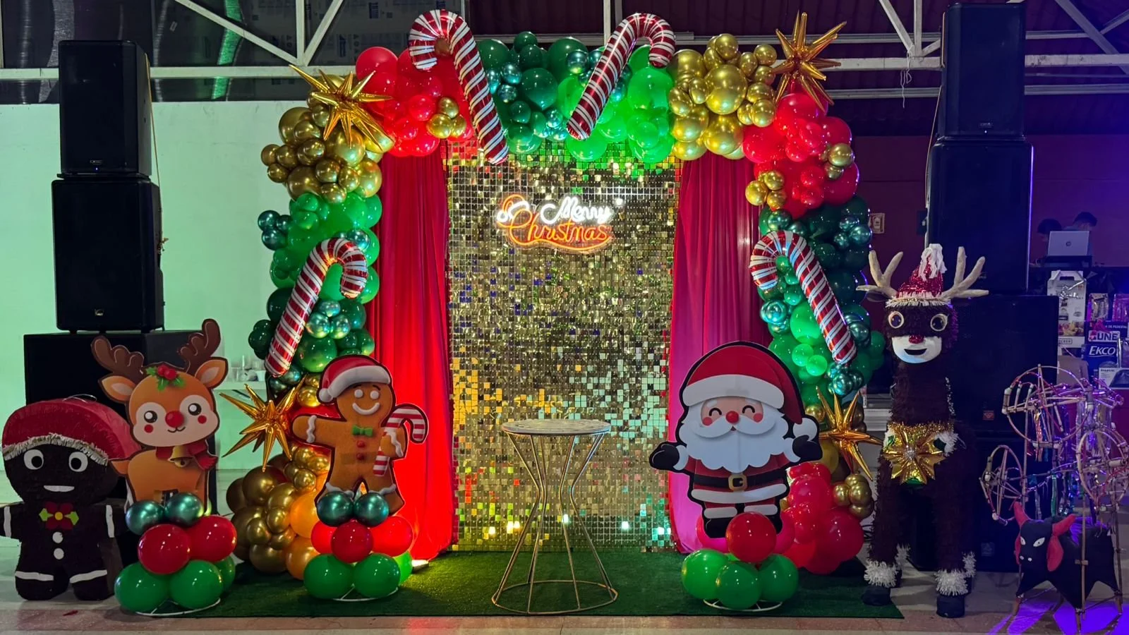 Decoración navideña con globo de arpillera y figuras festivas, incluyendo Santa Claus, reno, y chocolate, en un escenario con fondo de espejos dorados y luces verdes y rojas.