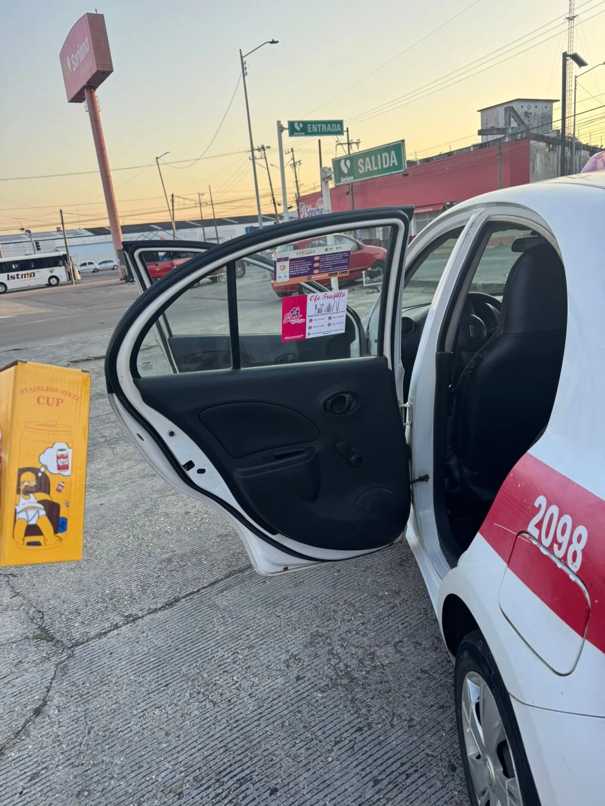 Interior del automóvil del servicio de transporte con la puerta abierta, en un lugar con señalización de entrada y salida, y anuncios publicitarios en el parabrisas y exterior.